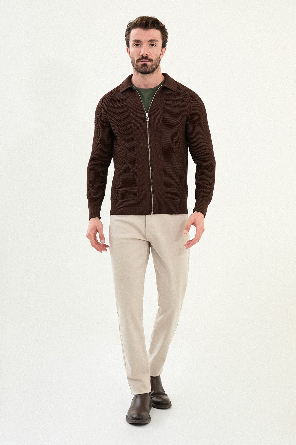 A man wearing a slim fit brown ribbed zip cardigan with a polo collar, styled with beige trousers.