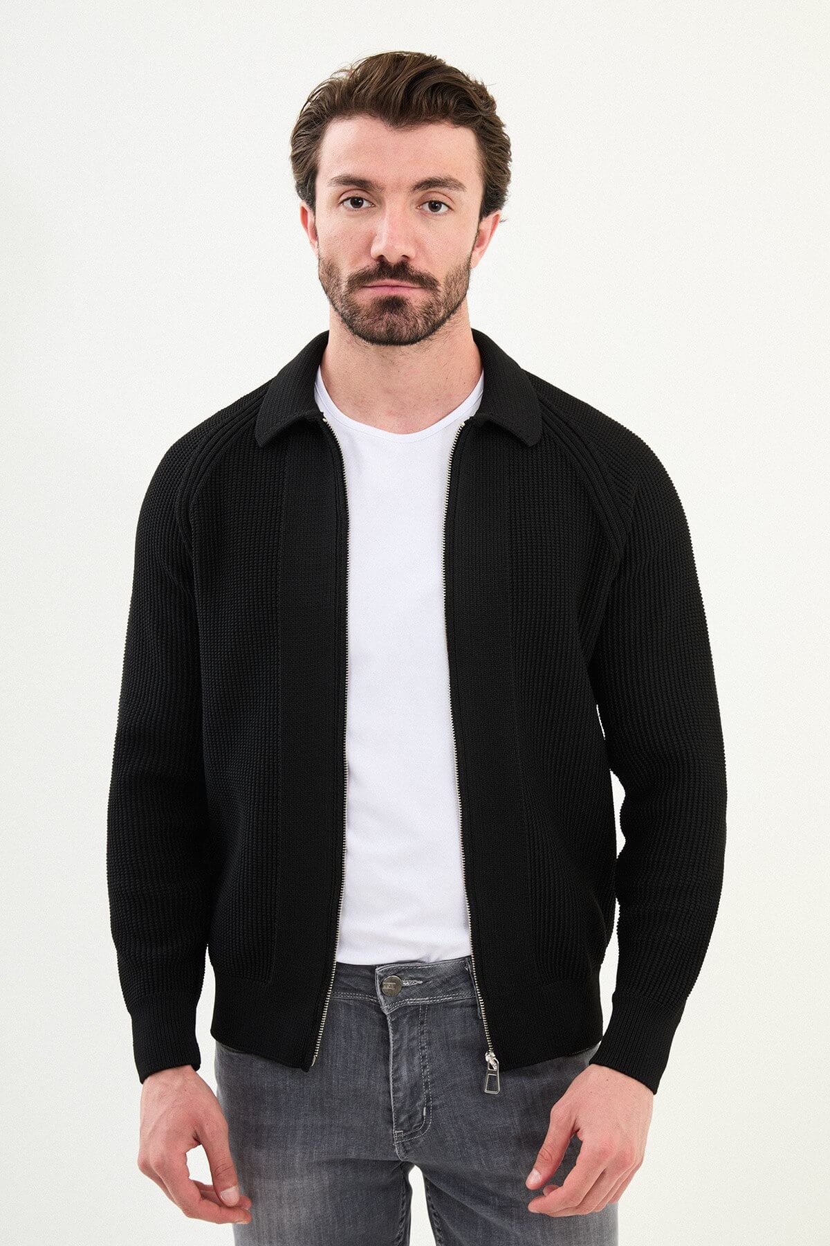 A man wearing a slim-fit black ribbed zip cardigan with a polo collar, styled with a white T-shirt and grey jeans.