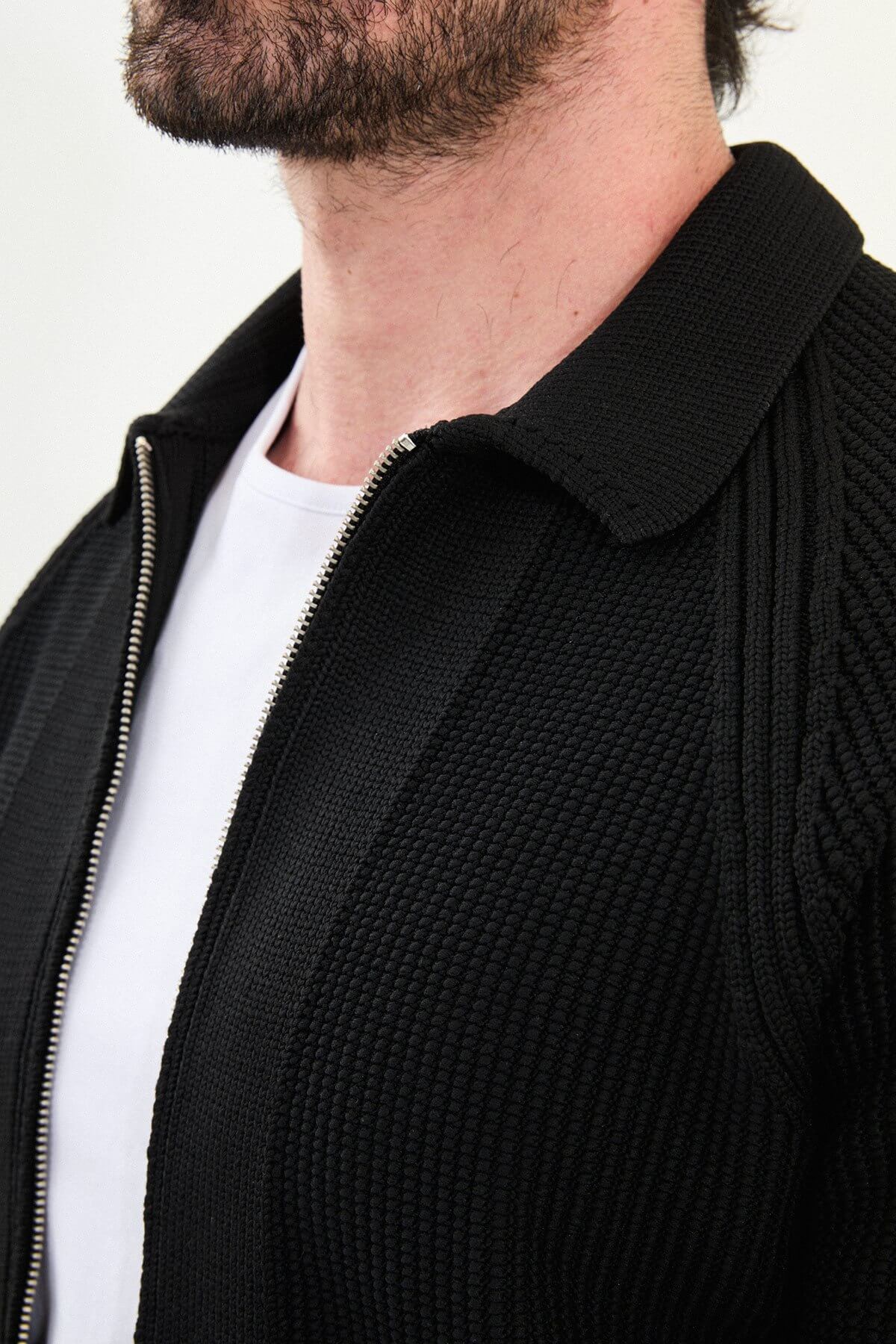 A man wearing a slim-fit black ribbed zip cardigan with a polo collar, styled with a white T-shirt and grey jeans.