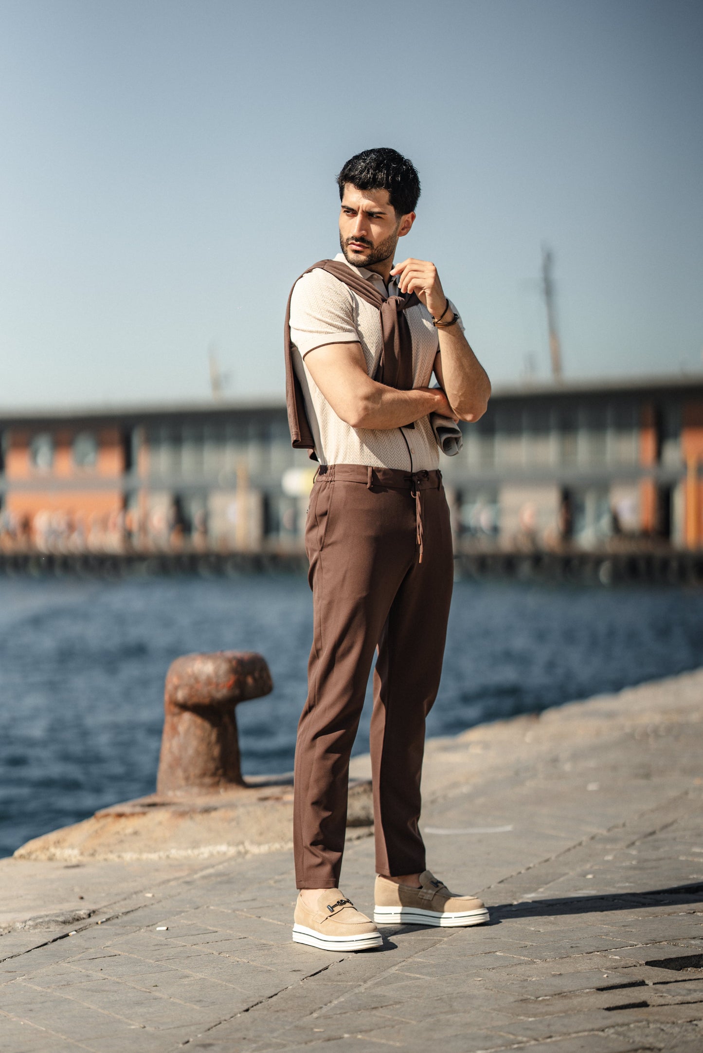 Man wearing the HolloMen Maldives Beige Knitted Polo Shirt, styled with casual chinos and loafers, standing next to the ocean in a sunlit tropical setting.