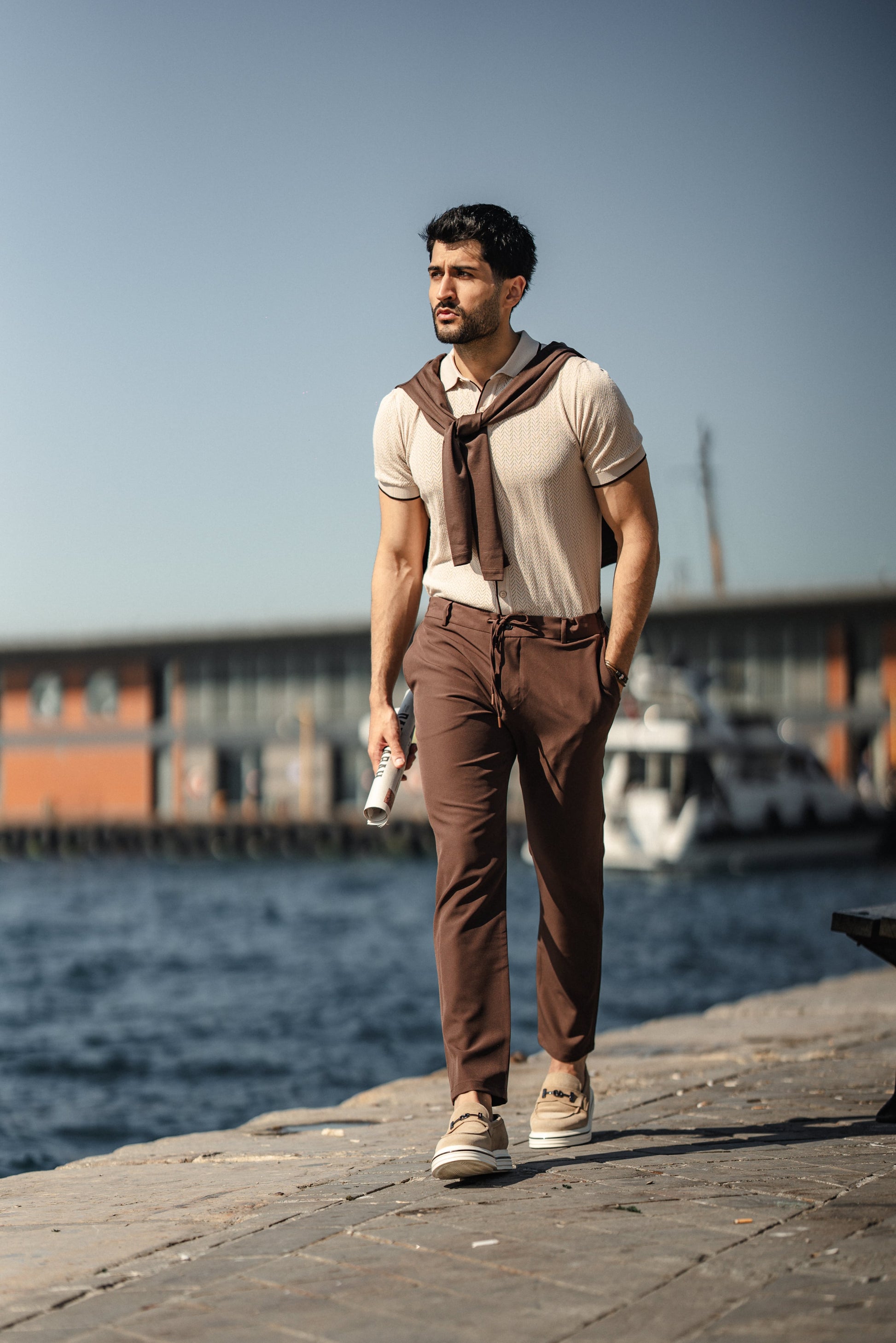 Man wearing the HolloMen Maldives Beige Knitted Polo Shirt, styled with casual chinos and loafers, standing next to the ocean in a sunlit tropical setting.