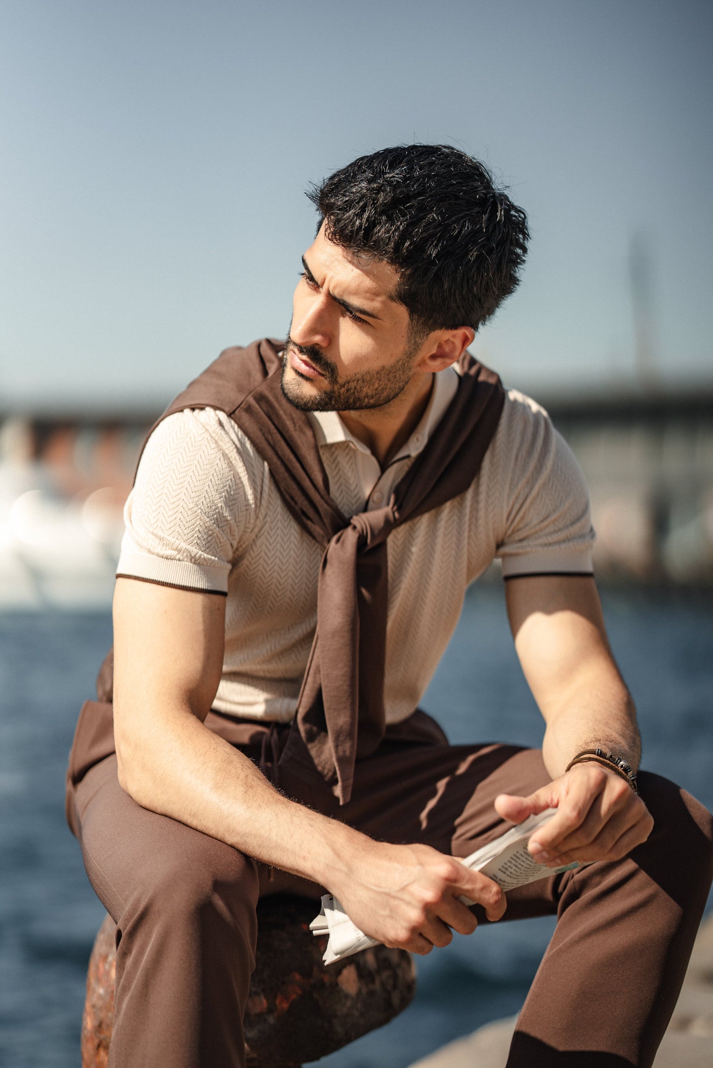 Man wearing the HolloMen Maldives Beige Knitted Polo Shirt, styled with casual chinos and loafers, standing next to the ocean in a sunlit tropical setting.