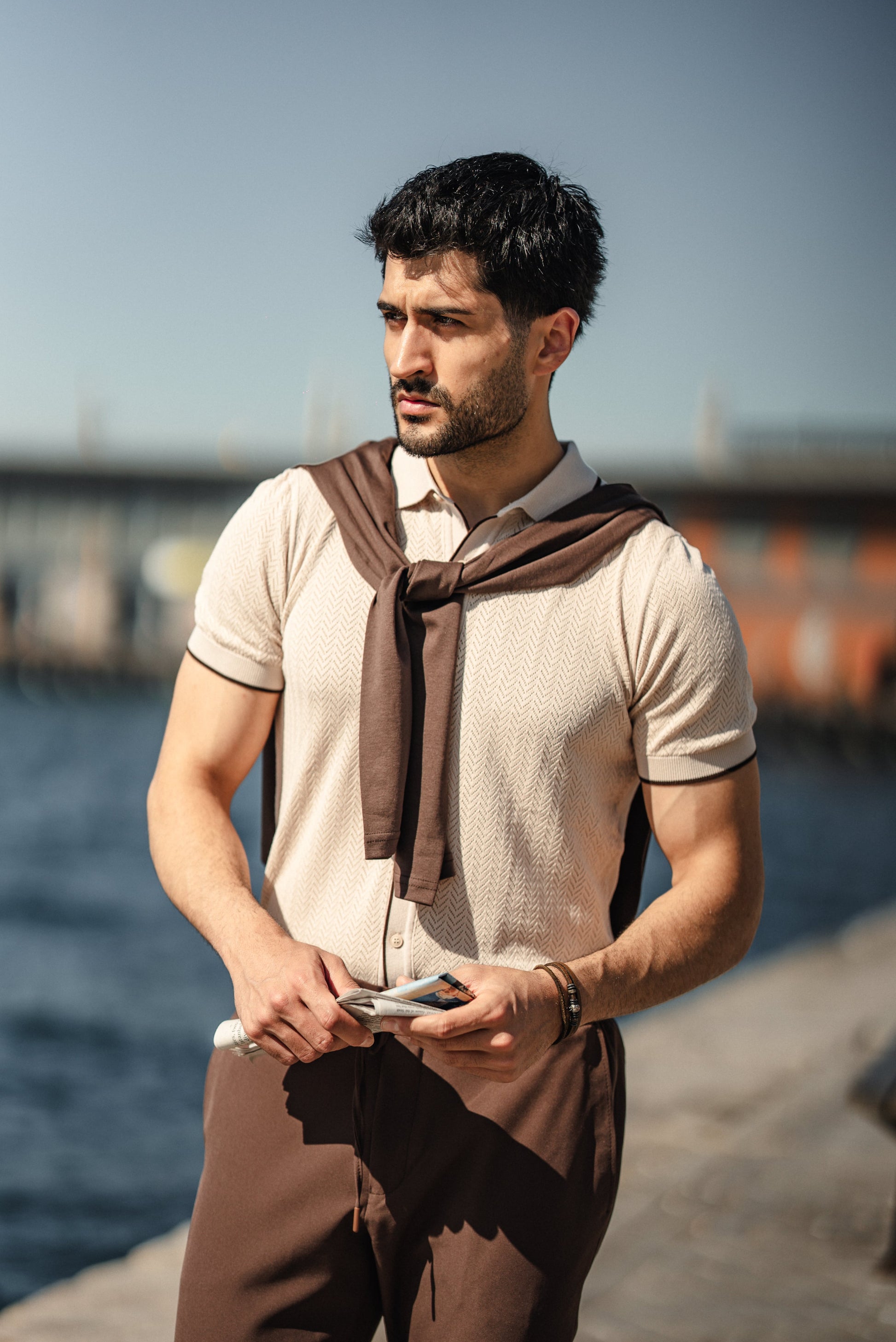 Man wearing the HolloMen Maldives Beige Knitted Polo Shirt, styled with casual chinos and loafers, standing next to the ocean in a sunlit tropical setting.