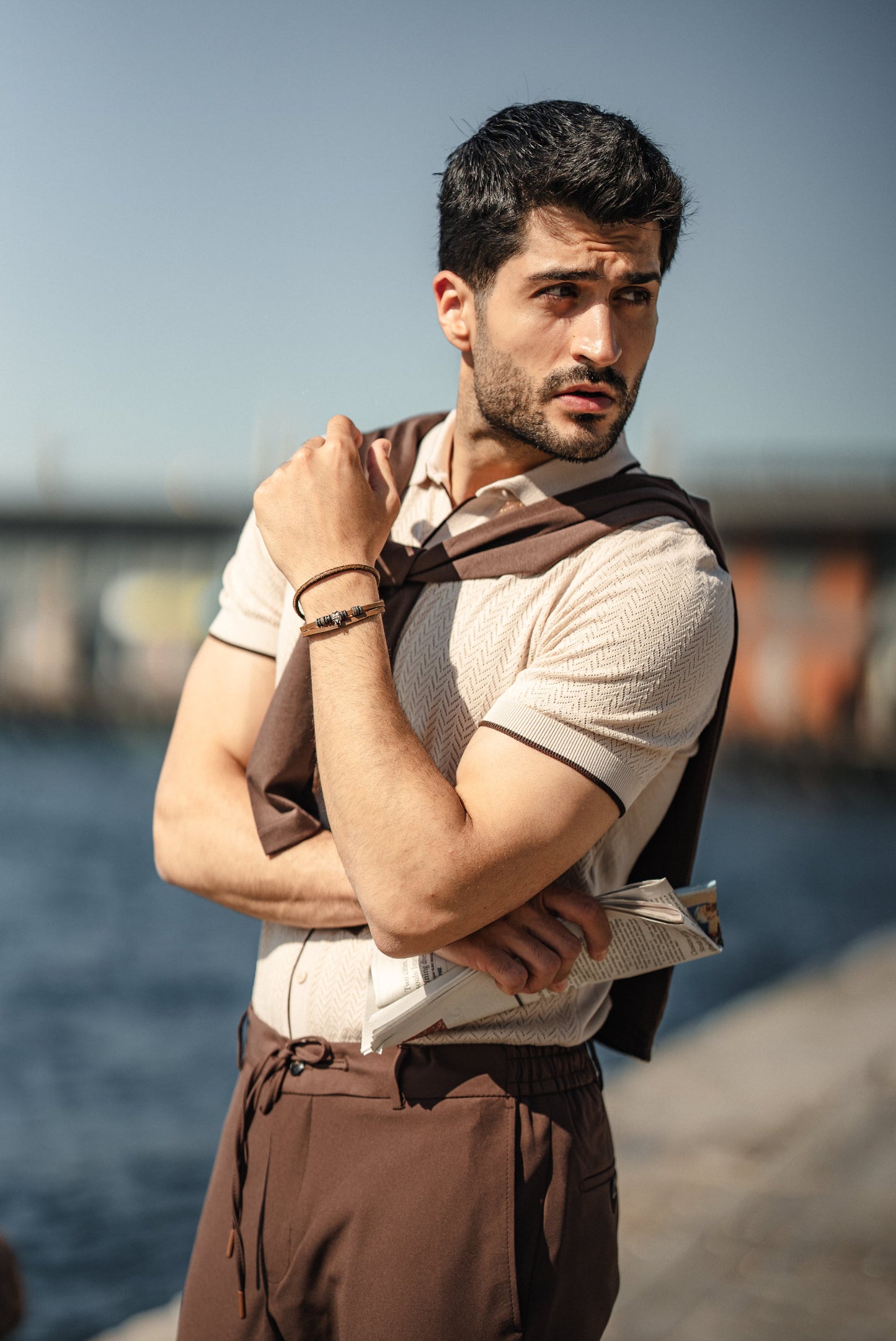 Man wearing the HolloMen Maldives Beige Knitted Polo Shirt, styled with casual chinos and loafers, standing next to the ocean in a sunlit tropical setting.
