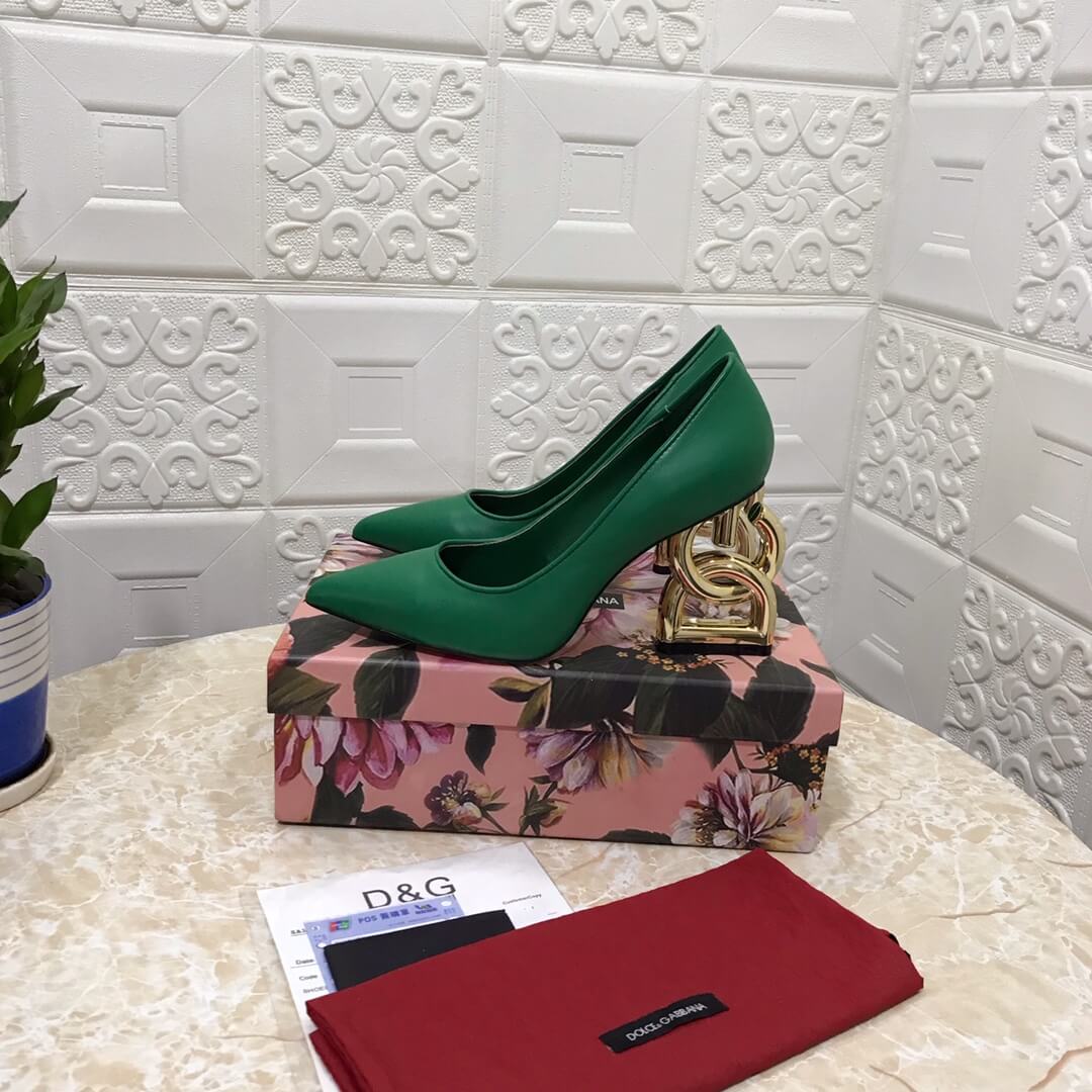 Close-up of Dolce & Gabbana pumps showcasing the sleek green leather, pointed toe, and the intricate, branded gold sculptural heel.

