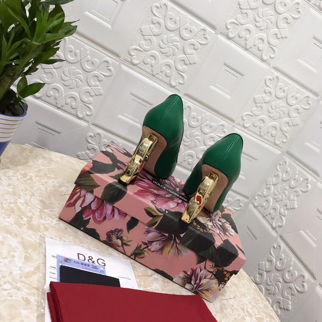 A pair of luxurious green Dolce & Gabbana high heels featuring unique gold "DG" heels, with one shoe placed on top of its box.

