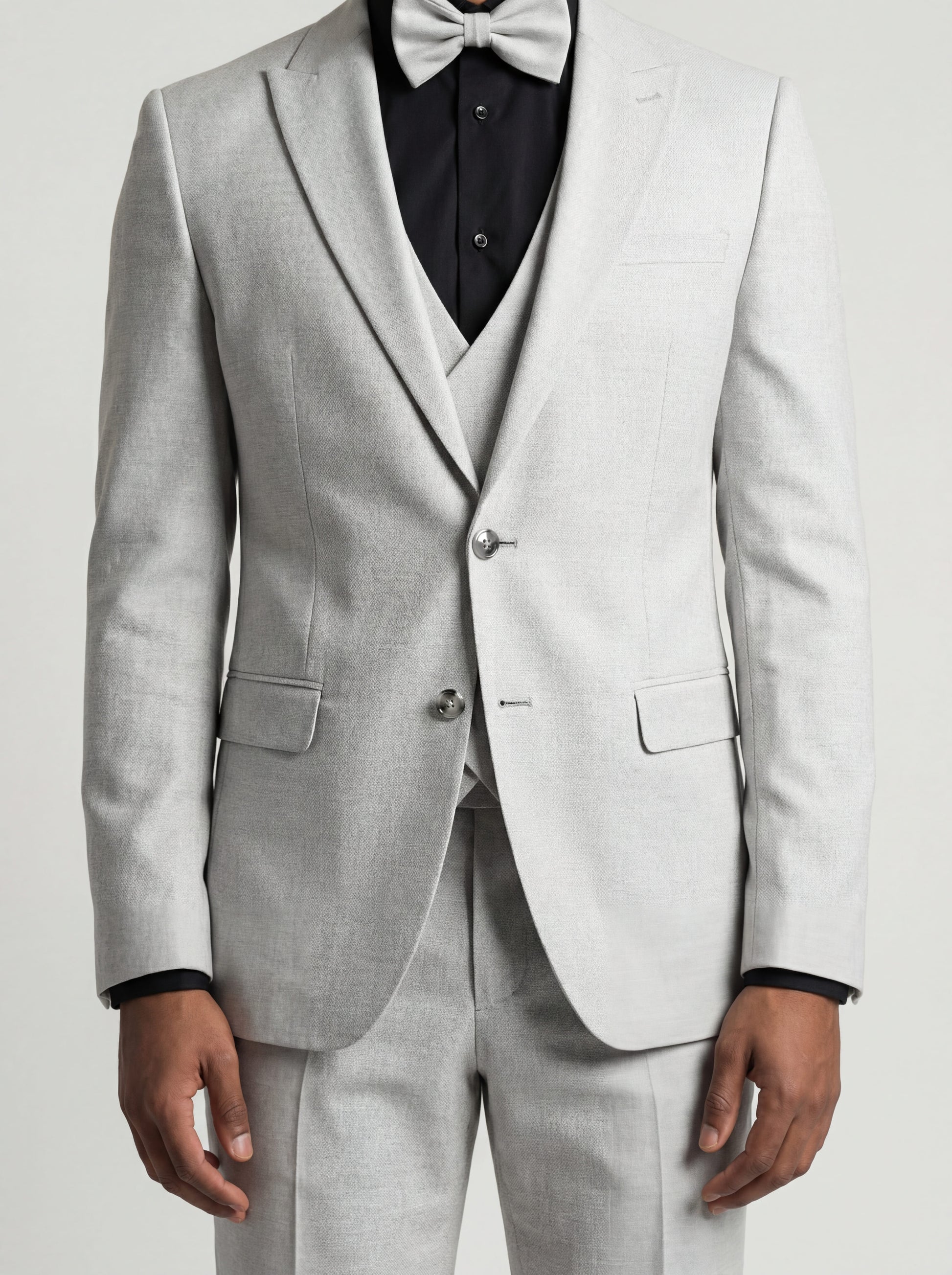 Young man wearing HolloMen's Gray Tuxedo Suit for prom, standing outdoors in a modern setting, featuring a black shirt and a stylish bow tie, showcasing a sleek and sophisticated look.