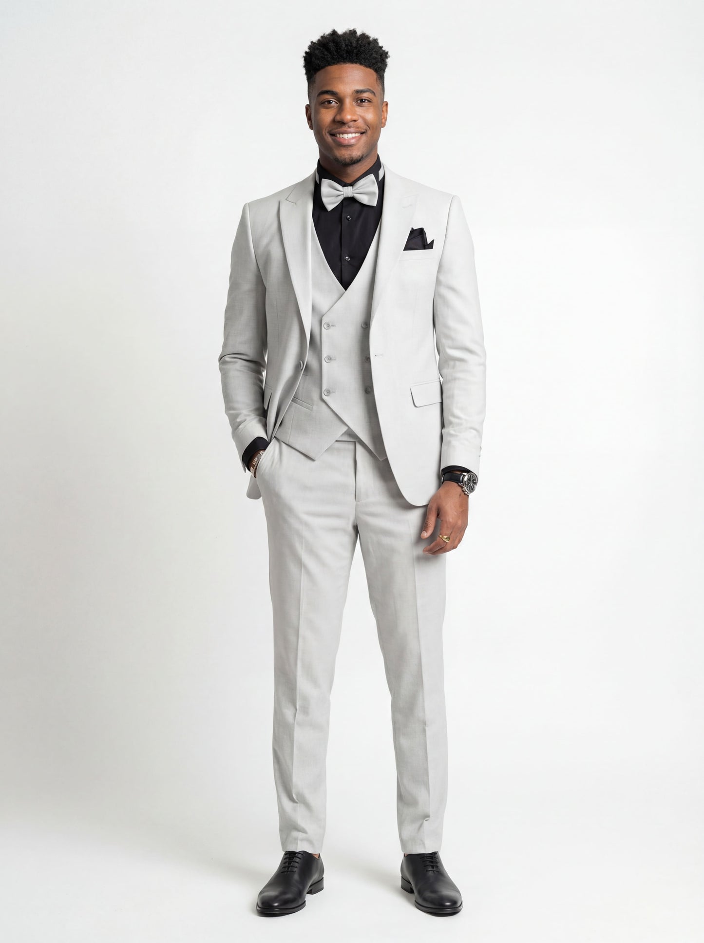 Young man wearing HolloMen's Gray Tuxedo Suit for prom, standing outdoors in a modern setting, featuring a black shirt and a stylish bow tie, showcasing a sleek and sophisticated look.