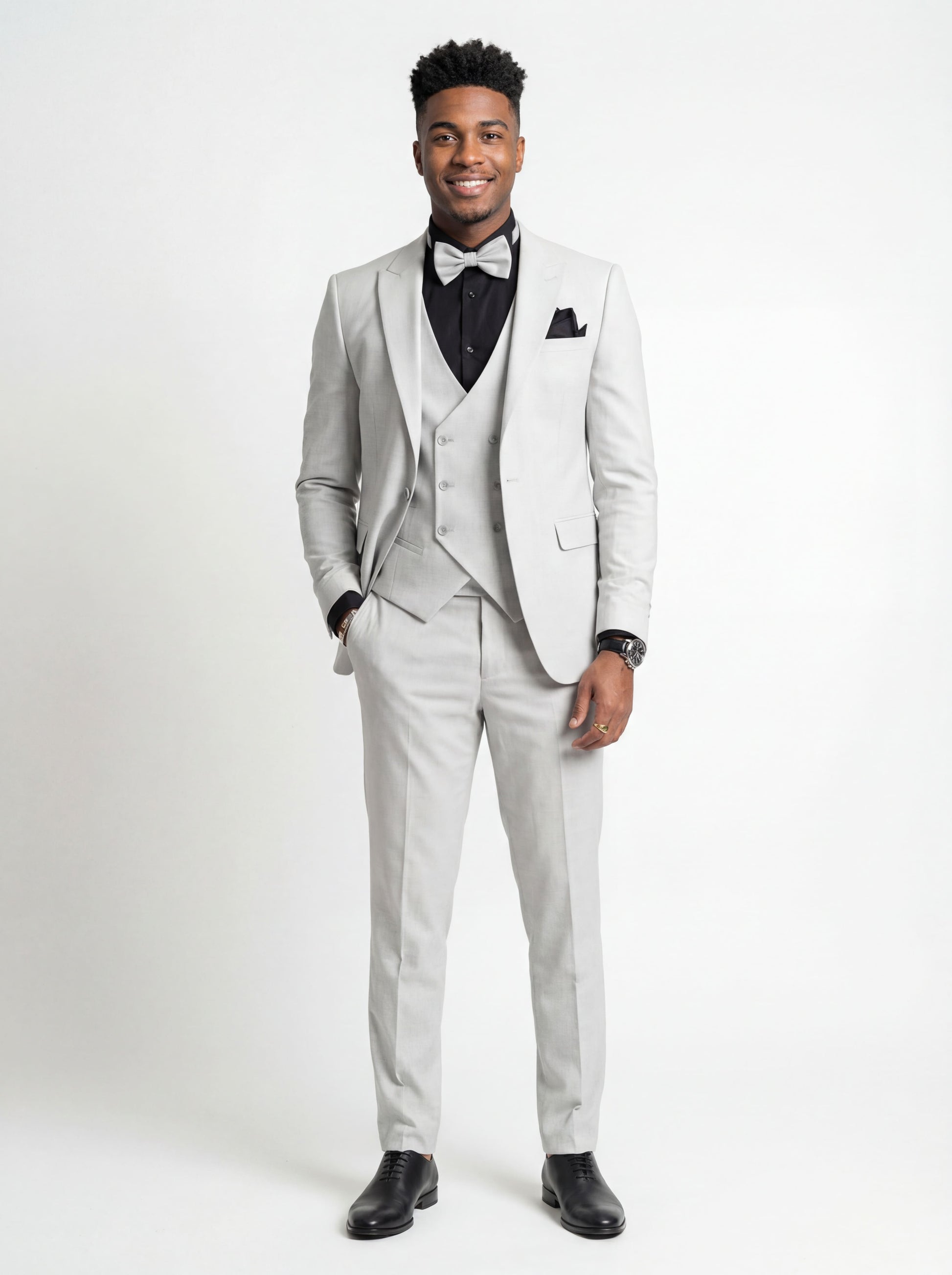 Young man wearing HolloMen's Gray Tuxedo Suit for prom, standing outdoors in a modern setting, featuring a black shirt and a stylish bow tie, showcasing a sleek and sophisticated look.