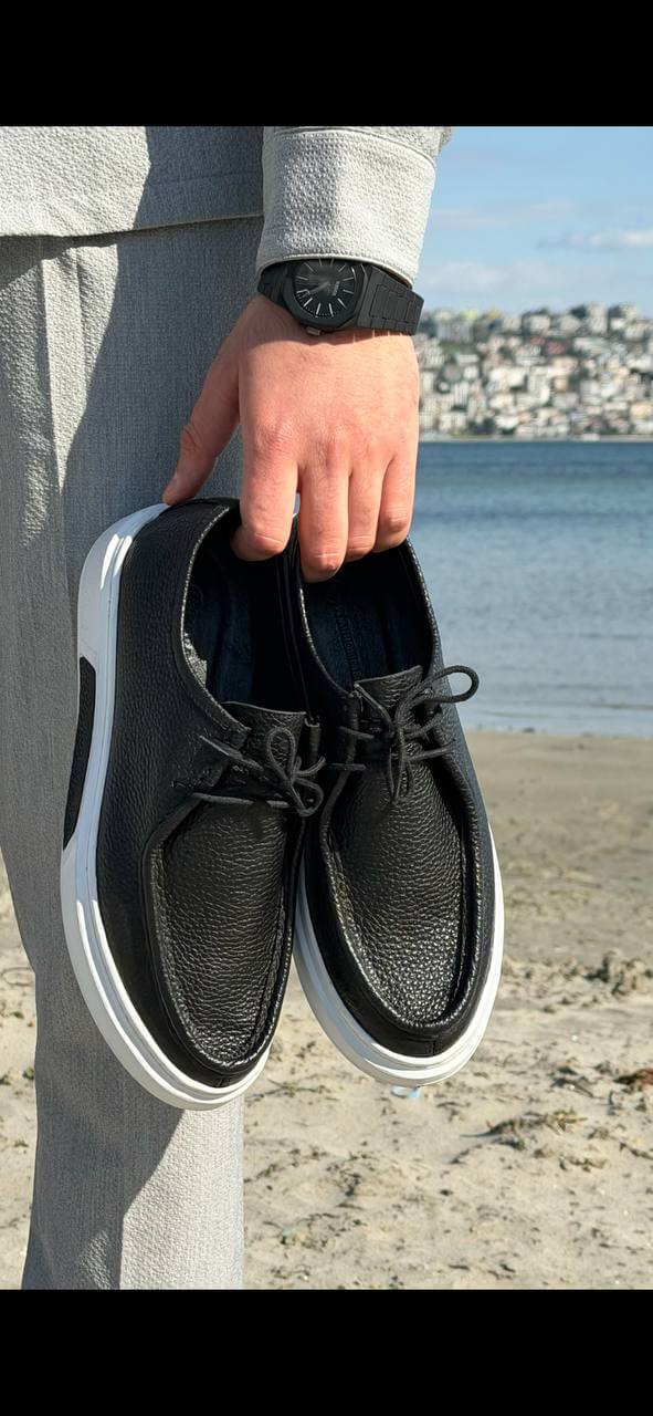 Men’s black leather casual derby shoes with white contrast EVA sole, held by hand in an outdoor setting, showcasing textured leather and lace-up design.