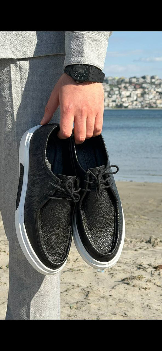 Men’s black leather casual derby shoes with white contrast EVA sole, held by hand in an outdoor setting, showcasing textured leather and lace-up design.