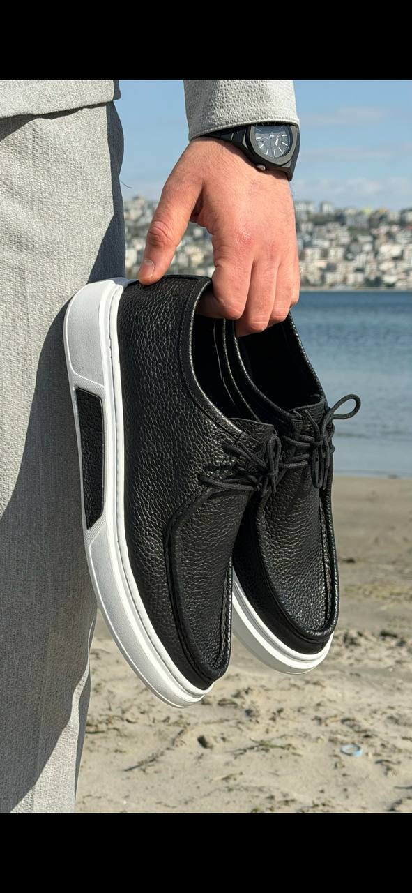 Men’s black leather casual derby shoes with white contrast EVA sole, held by hand in an outdoor setting, showcasing textured leather and lace-up design.