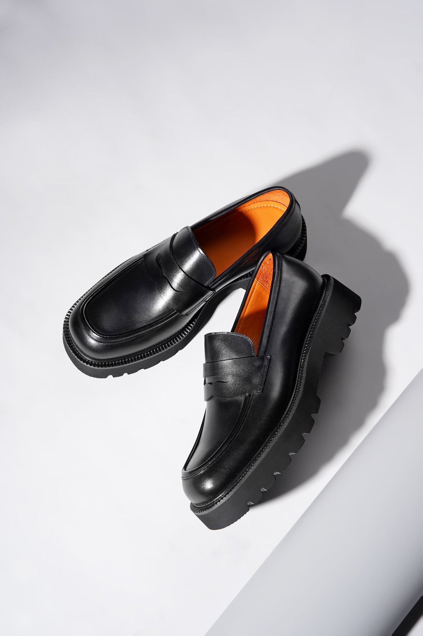 Stylish angled pair of black penny loafers with chunky sole and premium finish.