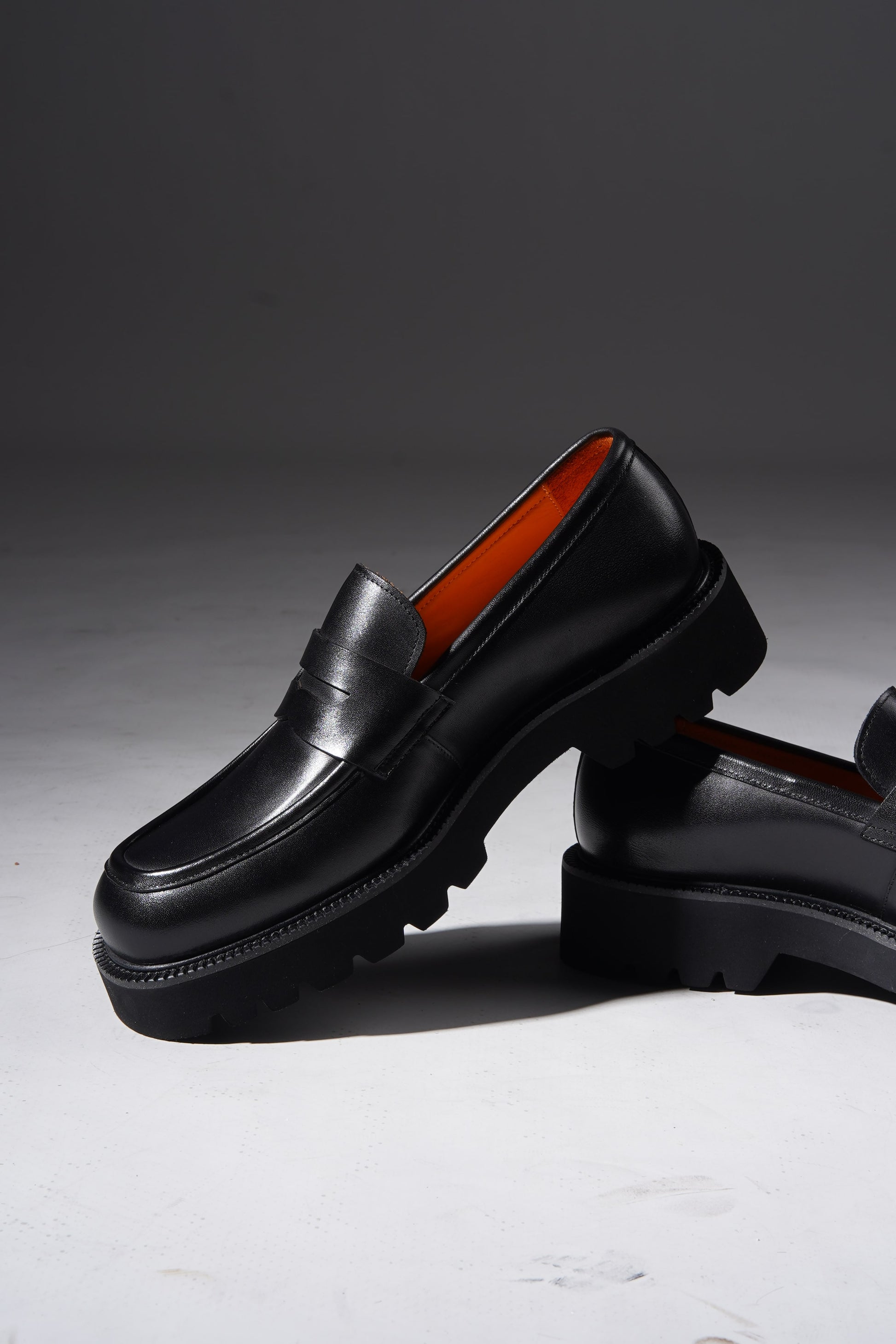 Stylish angled pair of black penny loafers with chunky sole and premium finish.