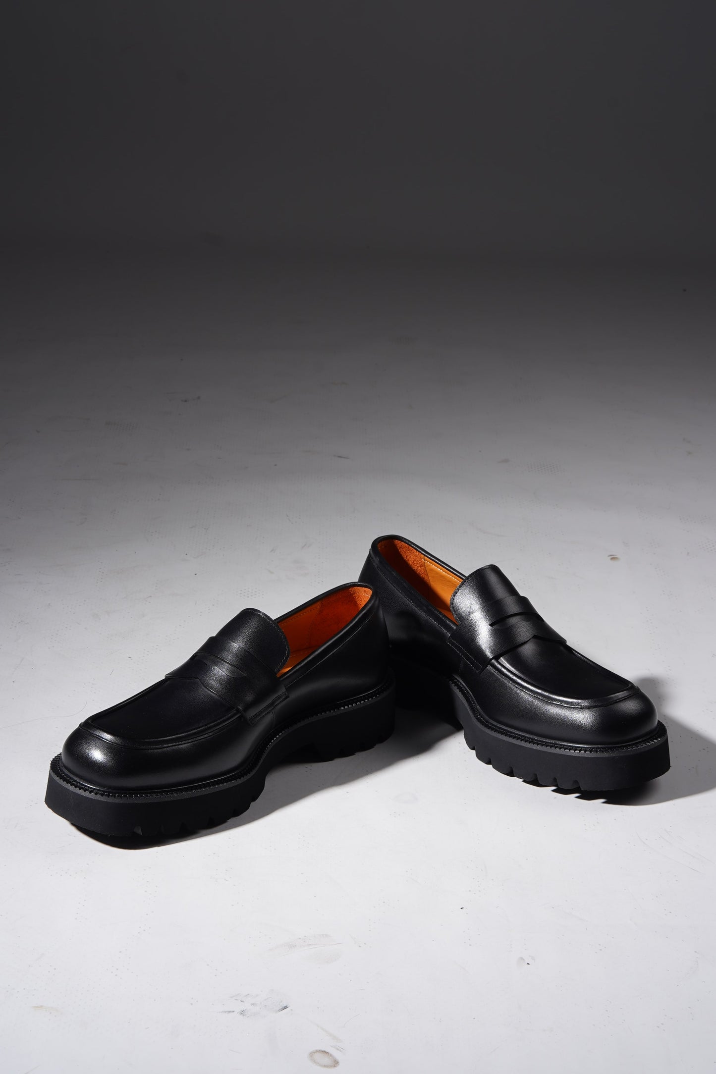 Stylish angled pair of black penny loafers with chunky sole and premium finish.