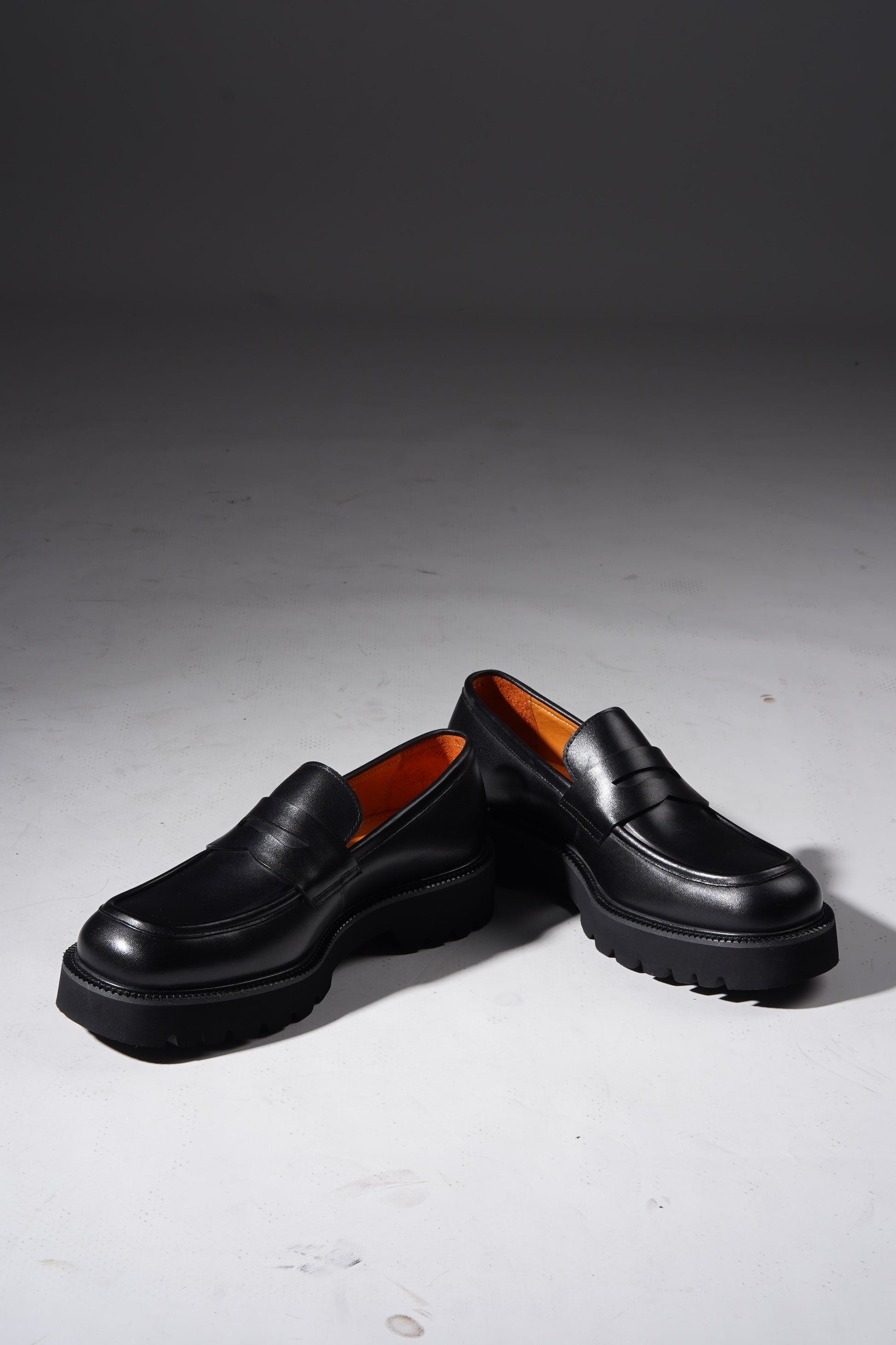 Stylish angled pair of black penny loafers with chunky sole and premium finish.