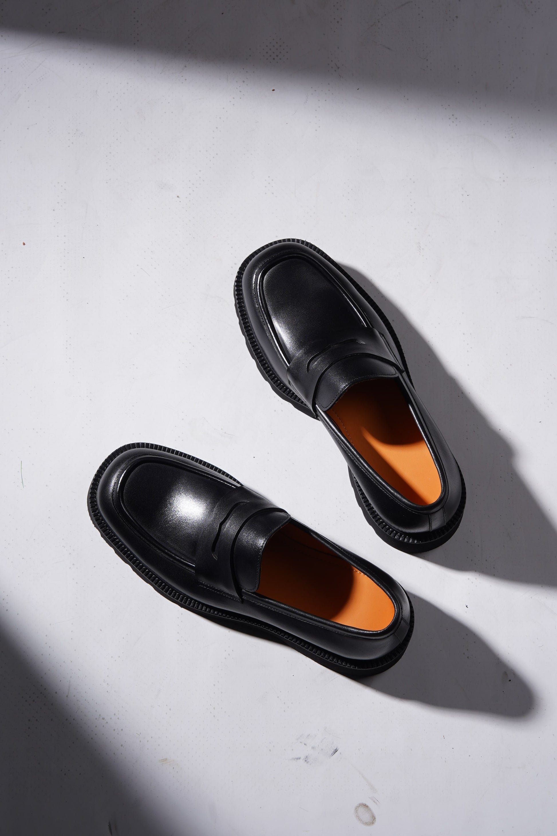Stylish angled pair of black penny loafers with chunky sole and premium finish.