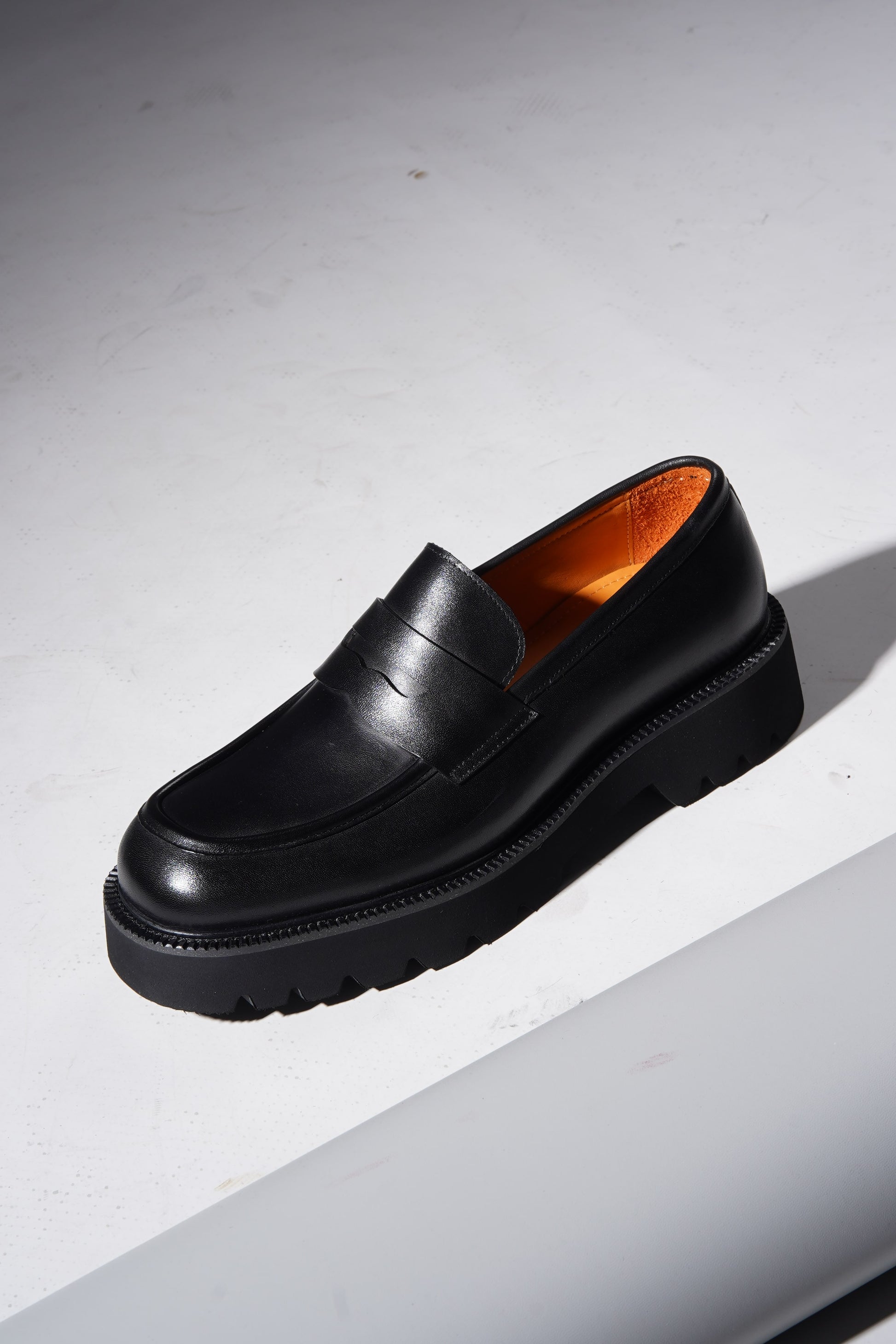 Stylish angled pair of black penny loafers with chunky sole and premium finish.
