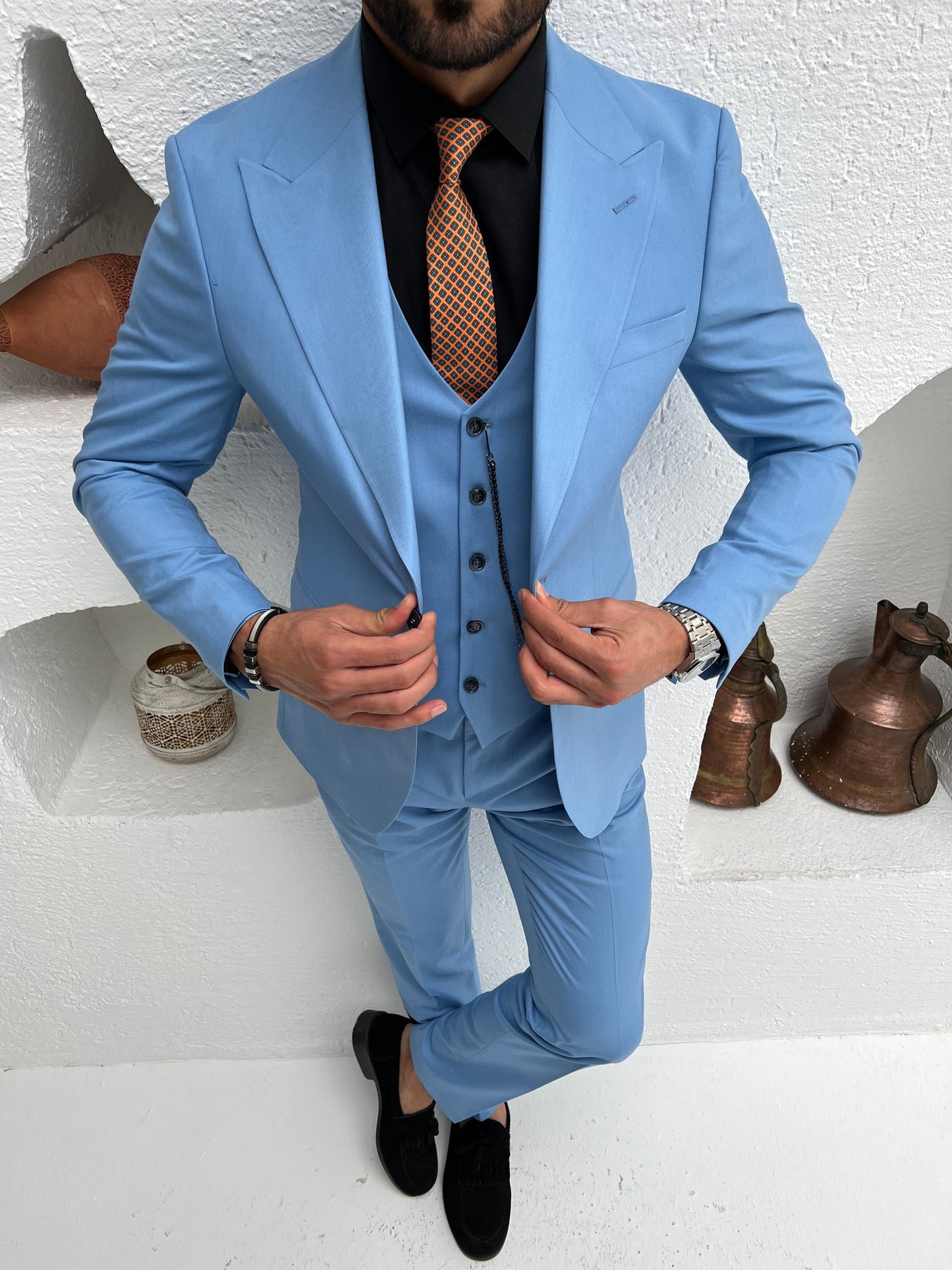 Men’s sky-blue slim-fit 3-piece suit with blazer, waistcoat, and trousers, styled with a white shirt and patterned tie in a modern interior setting.
