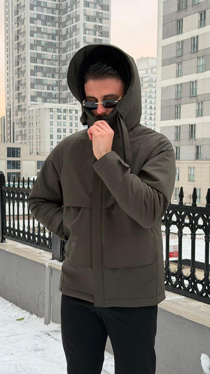 Men’s matte khaki technical winter parka with storm hood and reinforced chin guard, wind-resistant water-repellent polyester shell with stretch, oversized flap pockets and adjustable cuffs, urban commuter outerwear.