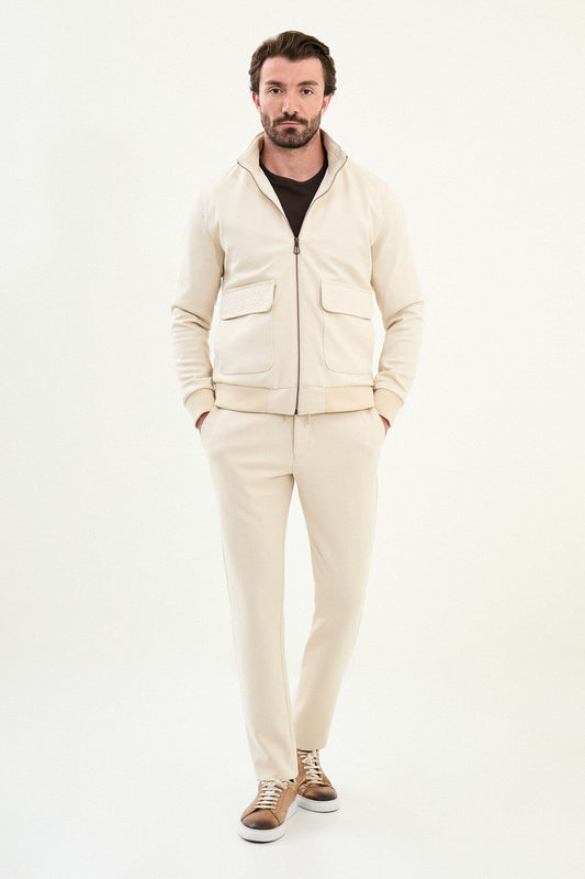 A male model wearing a beige slim fit jacket with zip closure and matching trousers, styled with brown sneakers.