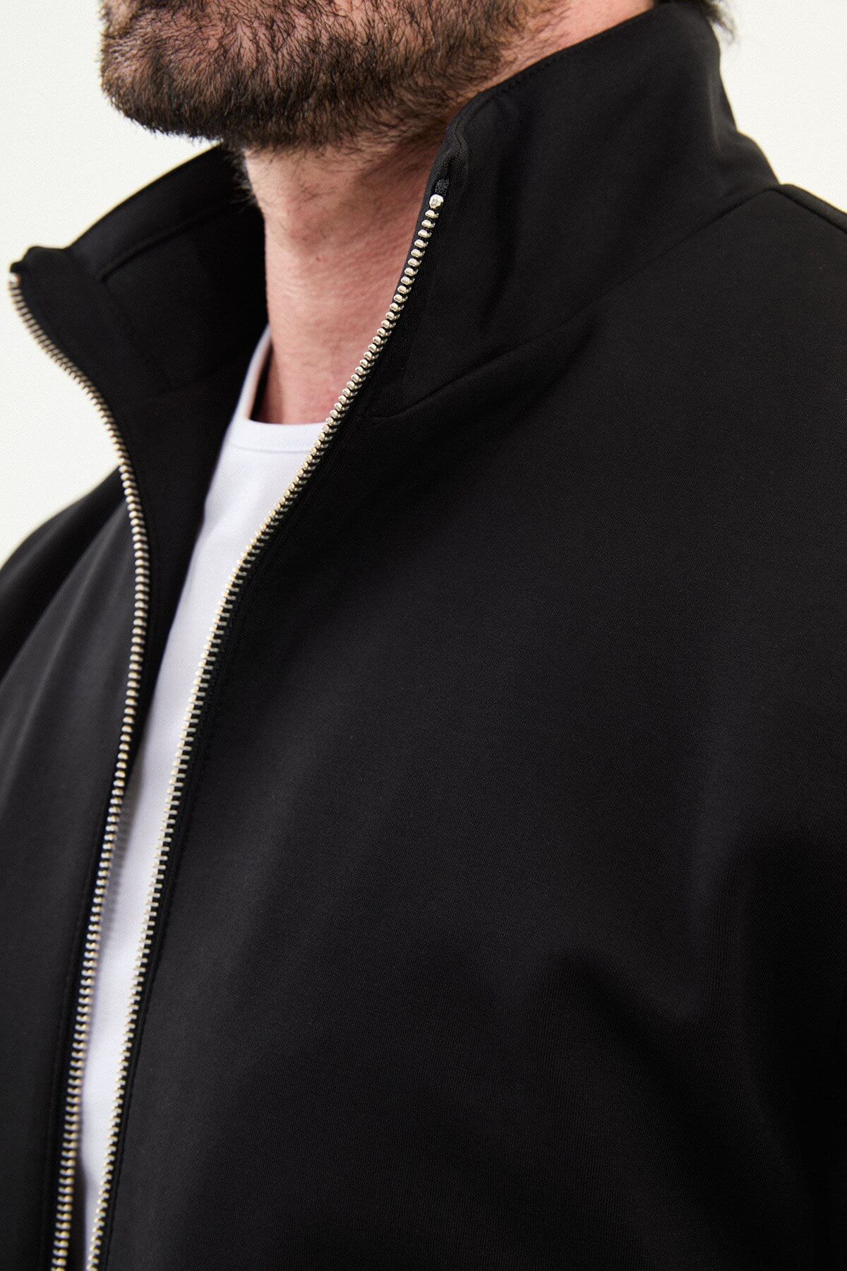 A man wearing a black slim fit knitwear jacket with flap pockets and matching black trousers.