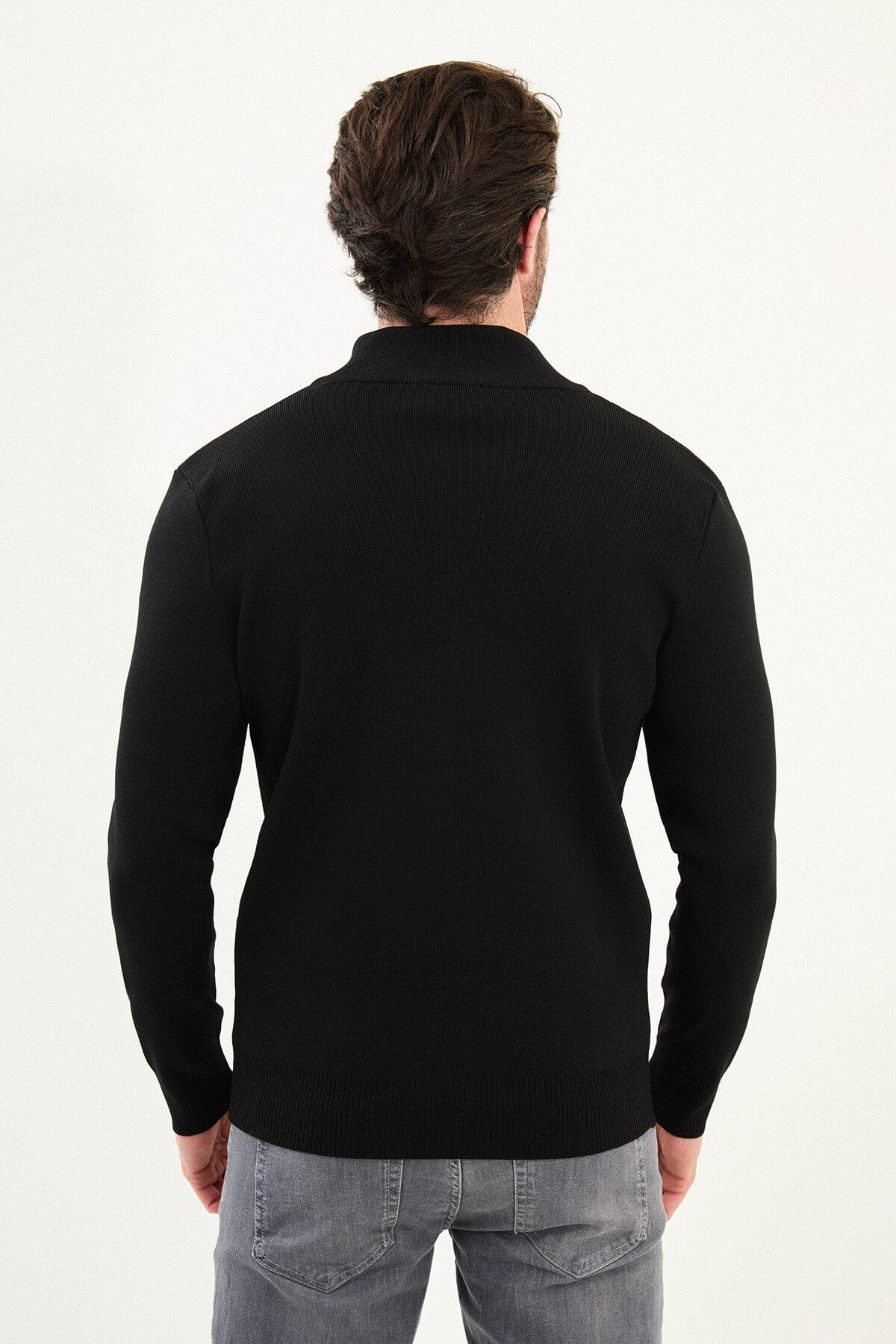 A man wearing a slim fit black zip cardigan over a white T-shirt, styled with grey jeans and black boots.