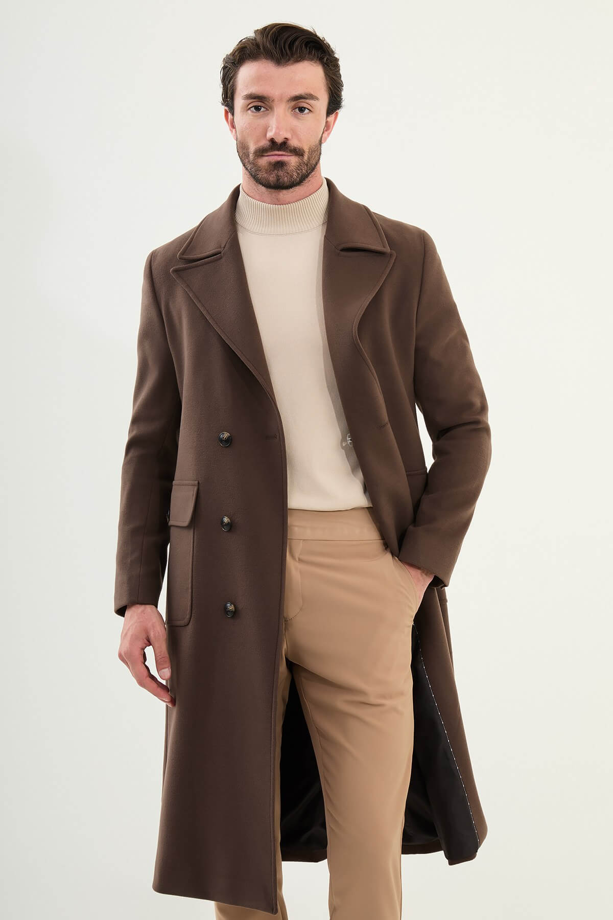 Full-body view of men’s brown slim fit double-breasted cachet coat styled with beige trousers and boots.