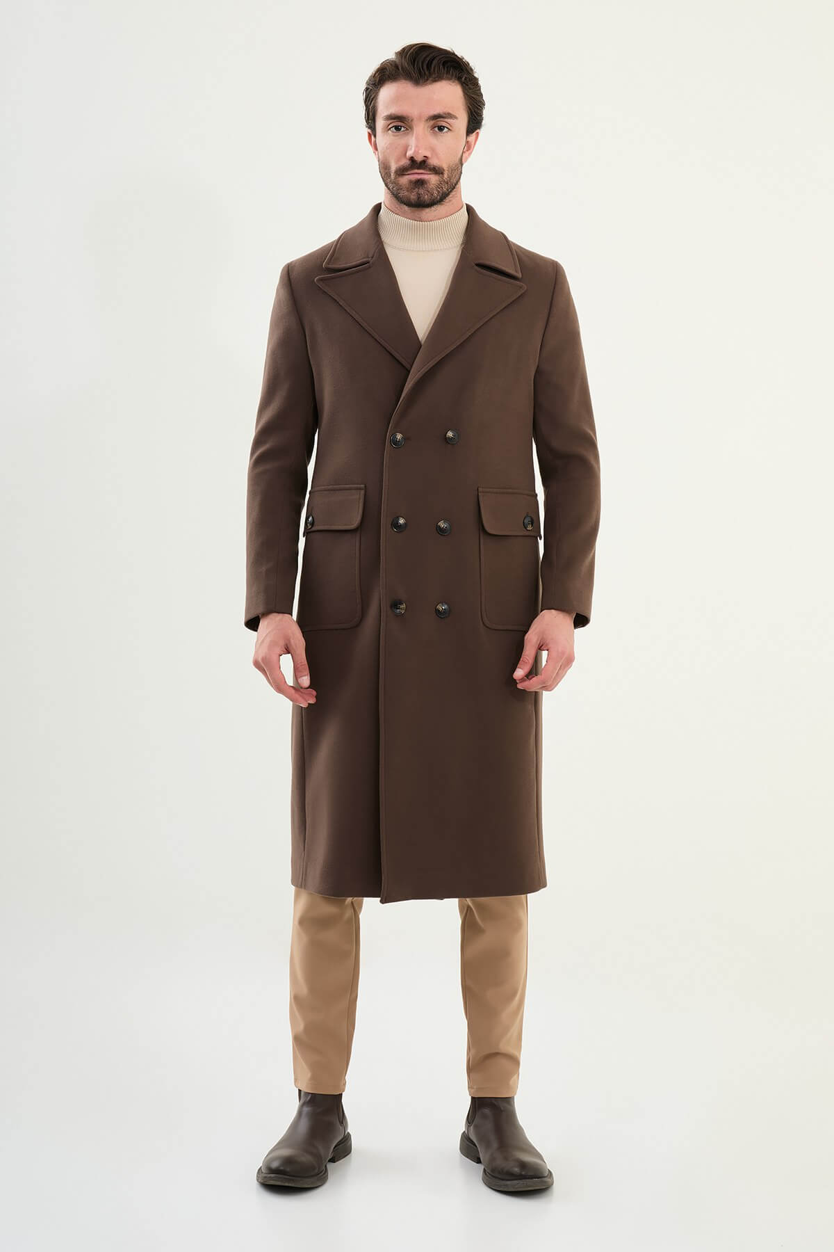 Full-body view of men’s brown slim fit double-breasted cachet coat styled with beige trousers and boots.