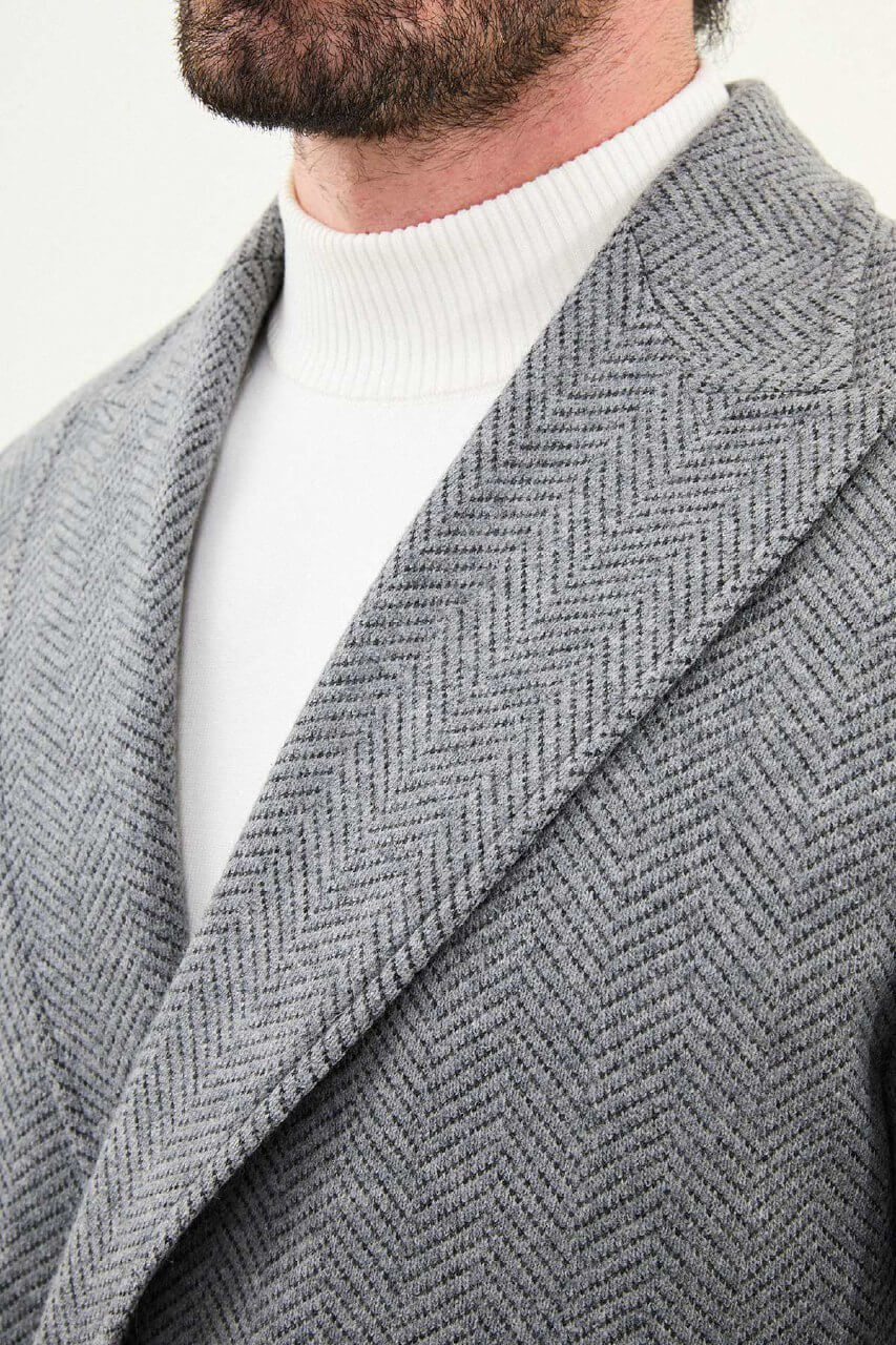 Full-body view of a man in a gray double-breasted slim fit coat, styled with black trousers and black leather boots.