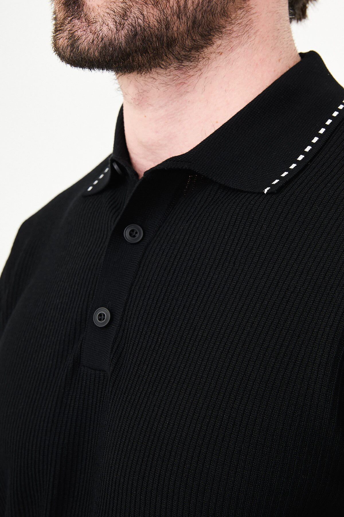 Man wearing black slim-fit quarter-zip polo t-shirt with white stripe accents, styled with white trousers.