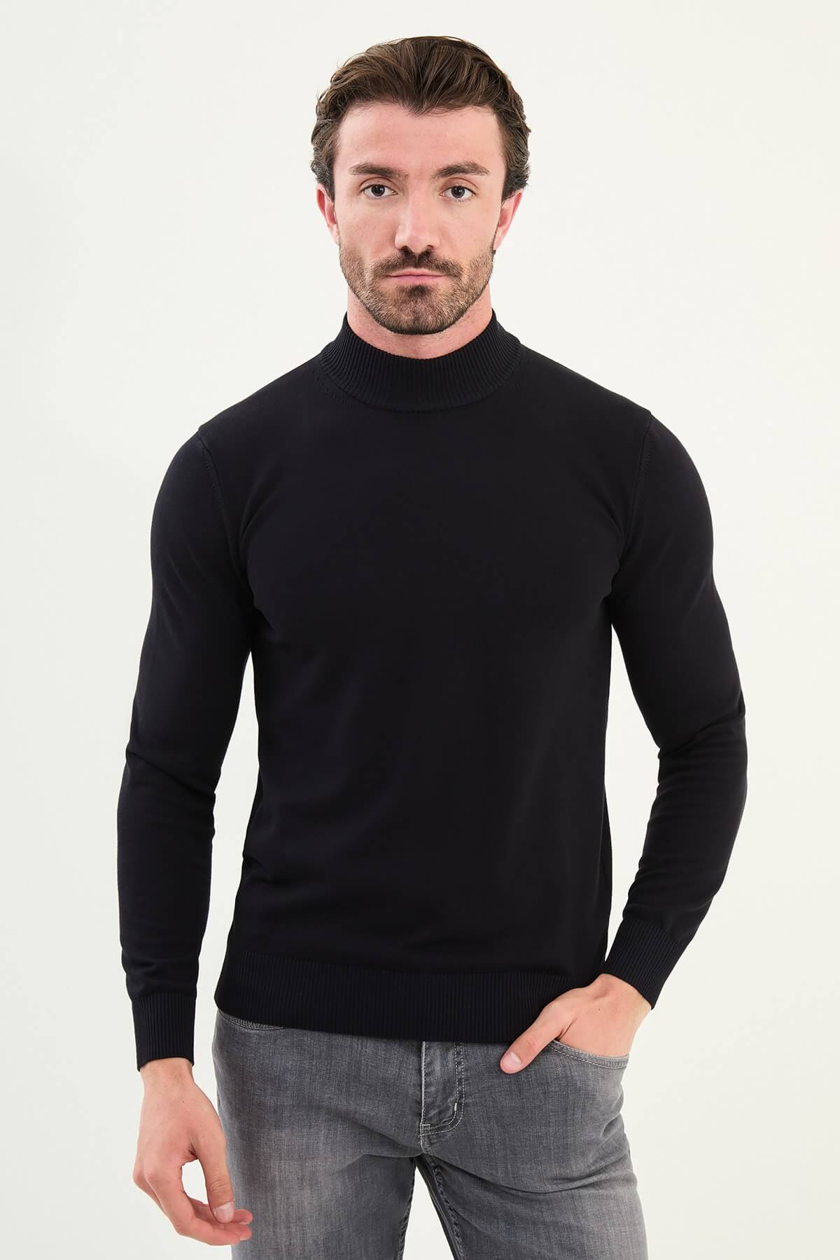 Man wearing a navy slim fit turtleneck knit sweater from the Fall-Winter collection, styled with grey jeans.