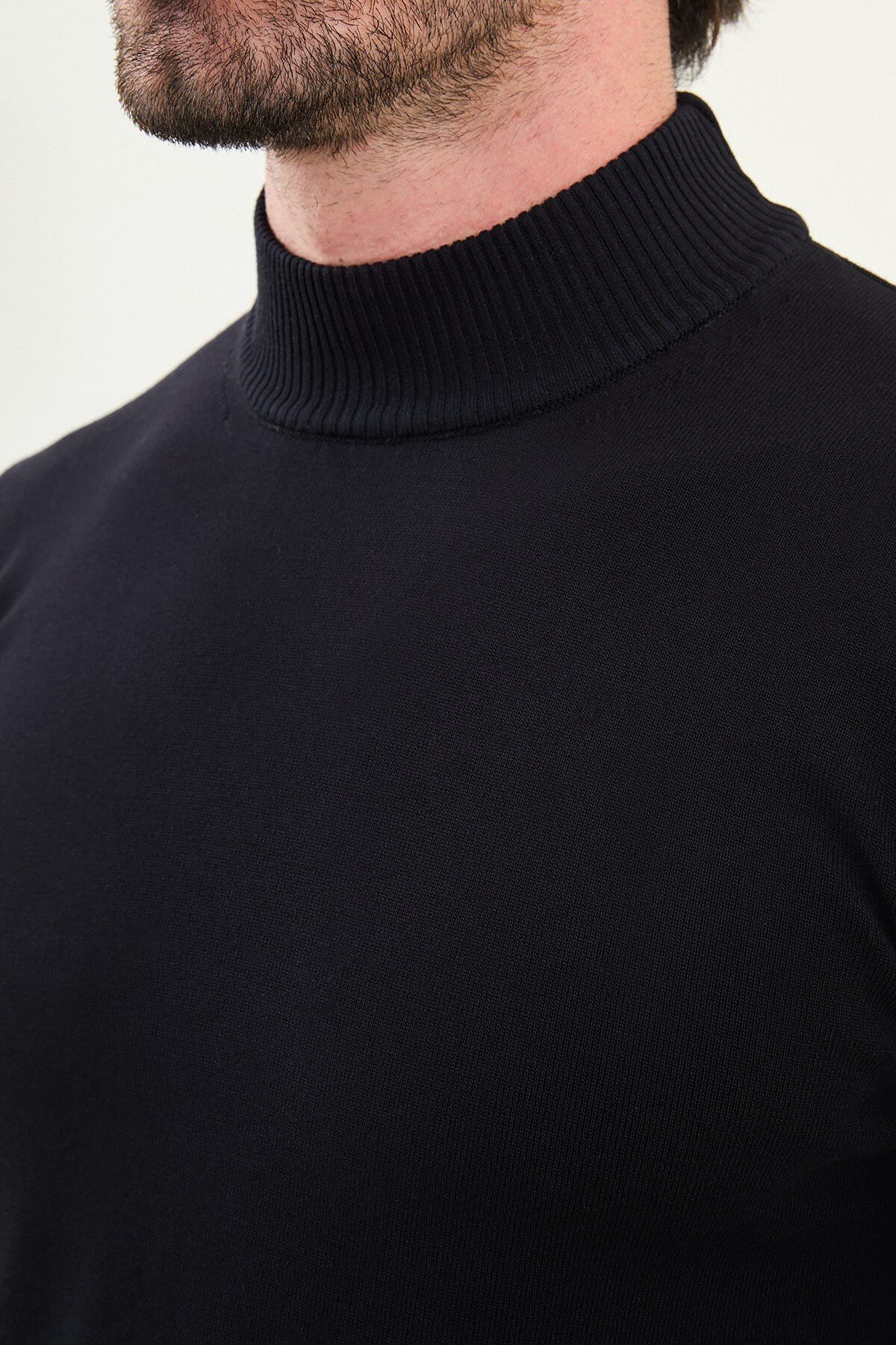Man wearing a navy slim fit turtleneck knit sweater from the Fall-Winter collection, styled with grey jeans.