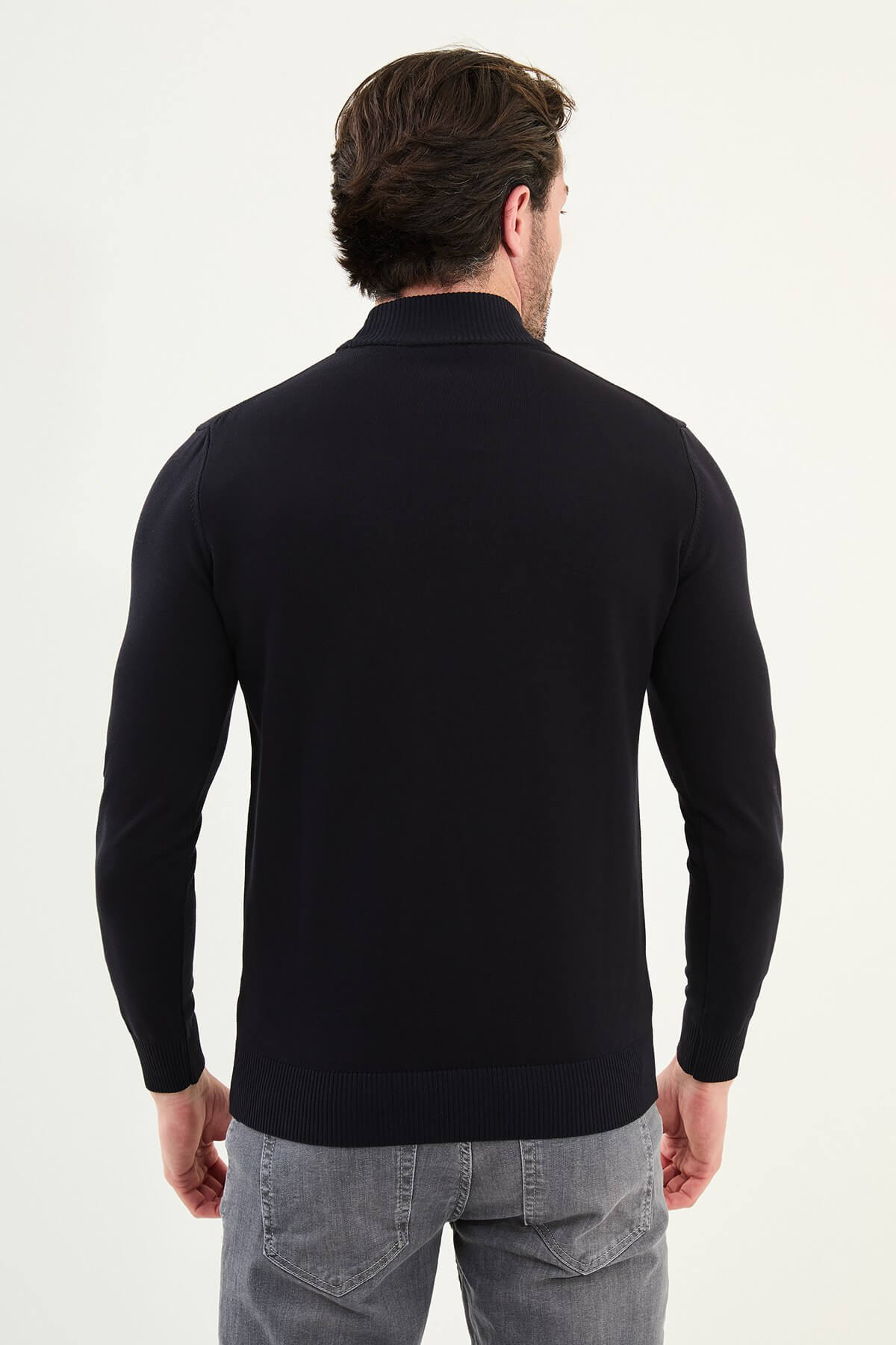 Man wearing a navy slim fit turtleneck knit sweater from the Fall-Winter collection, styled with grey jeans.