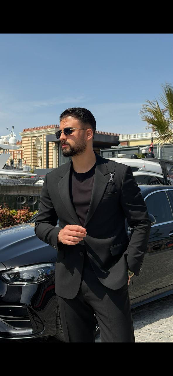 Men’s black slim fit suit with structured tailoring and harness detail, modern formal outfit styled with black shoes and minimal design