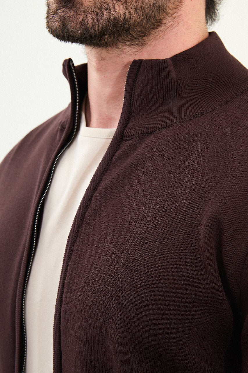 A man wearing a slim fit brown zip cardigan over a beige T-shirt, styled with light beige trousers.