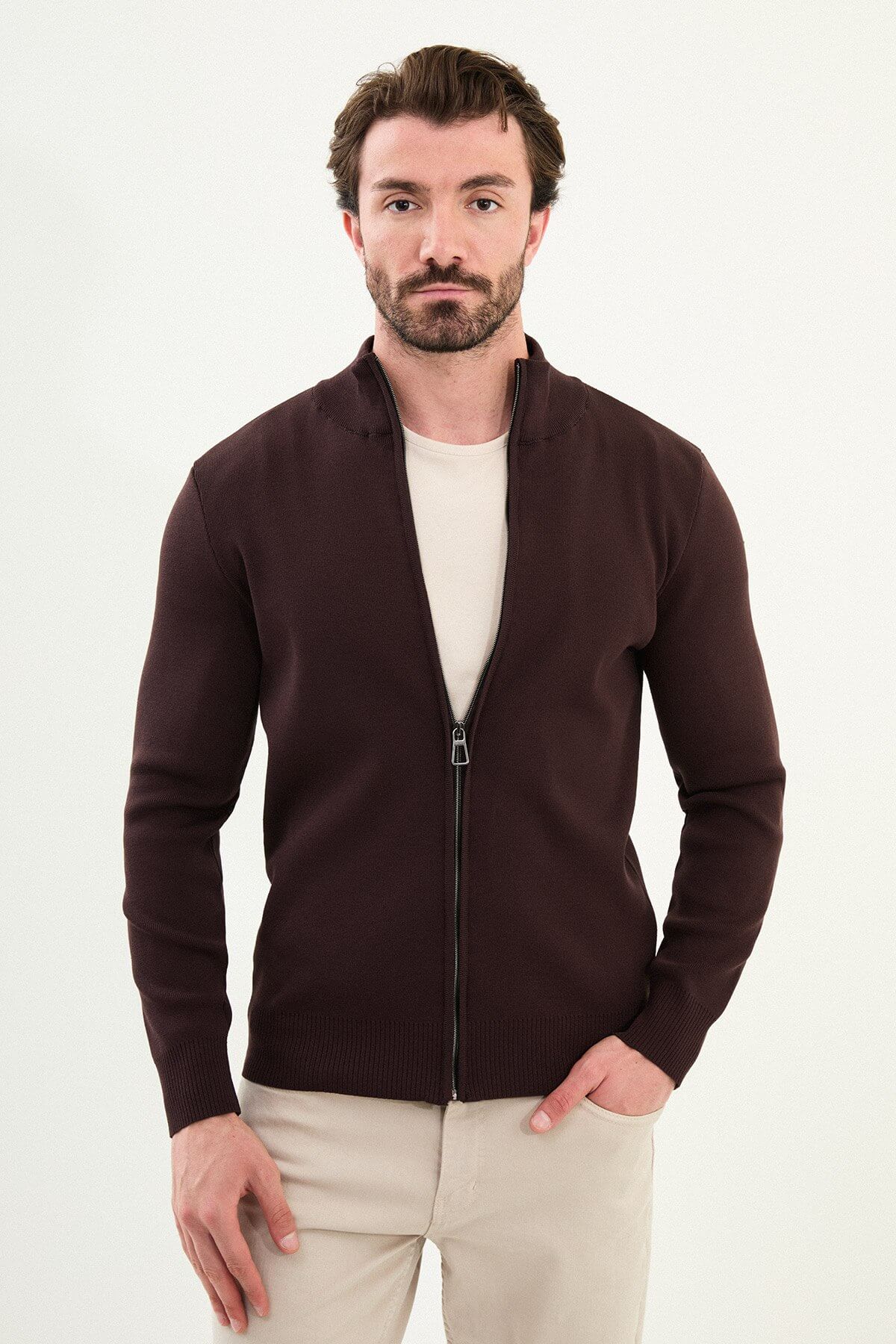 A man wearing a slim fit brown zip cardigan over a beige T-shirt, styled with light beige trousers.