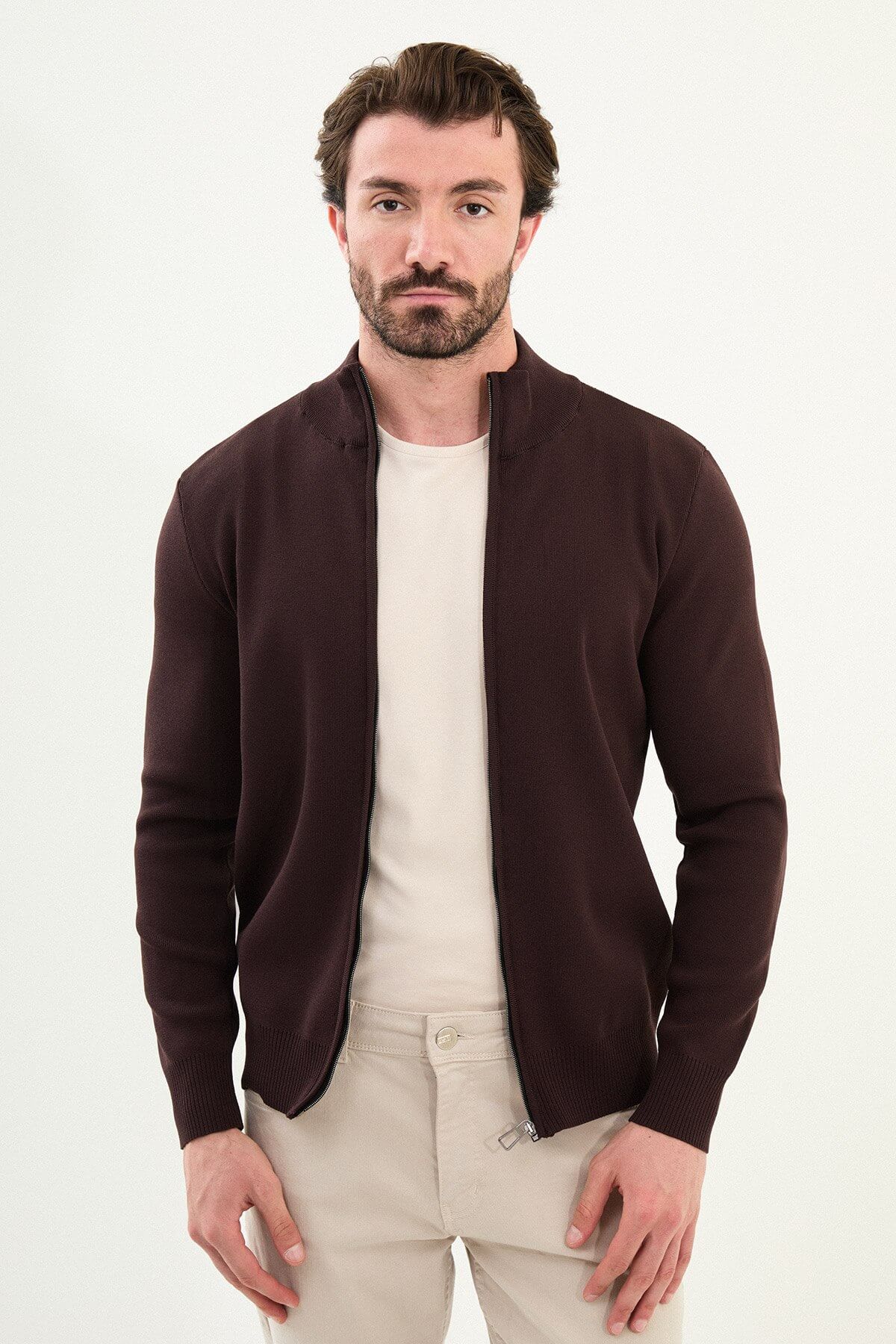 A man wearing a slim fit brown zip cardigan over a beige T-shirt, styled with light beige trousers.
