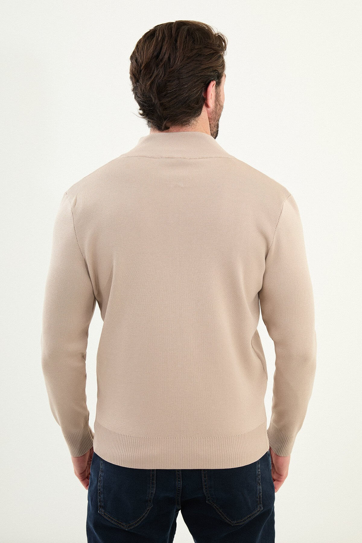 A man wearing a slim fit beige zip cardigan over a dark T-shirt, styled with dark navy jeans.