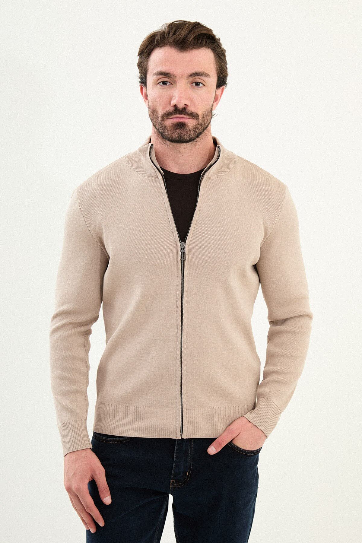 A man wearing a slim fit beige zip cardigan over a dark T-shirt, styled with dark navy jeans.