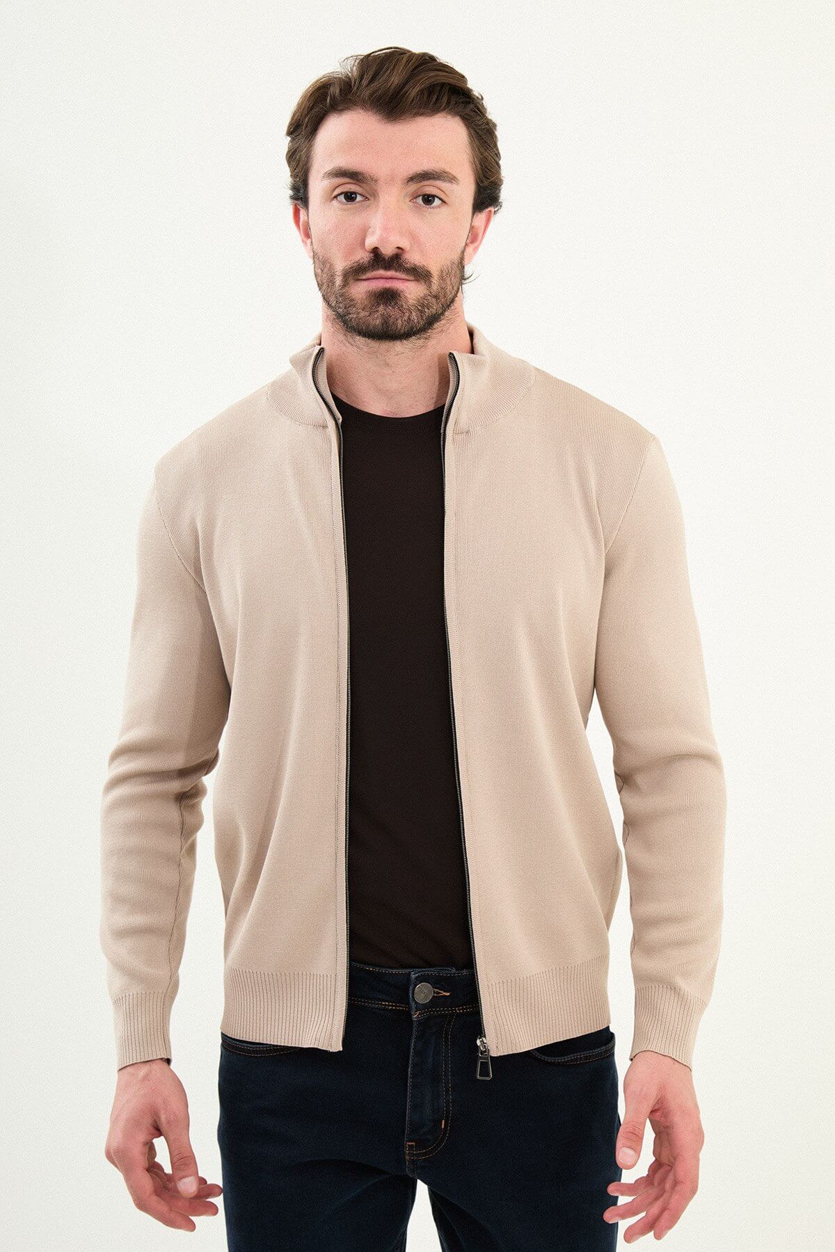A man wearing a slim fit beige zip cardigan over a dark T-shirt, styled with dark navy jeans.