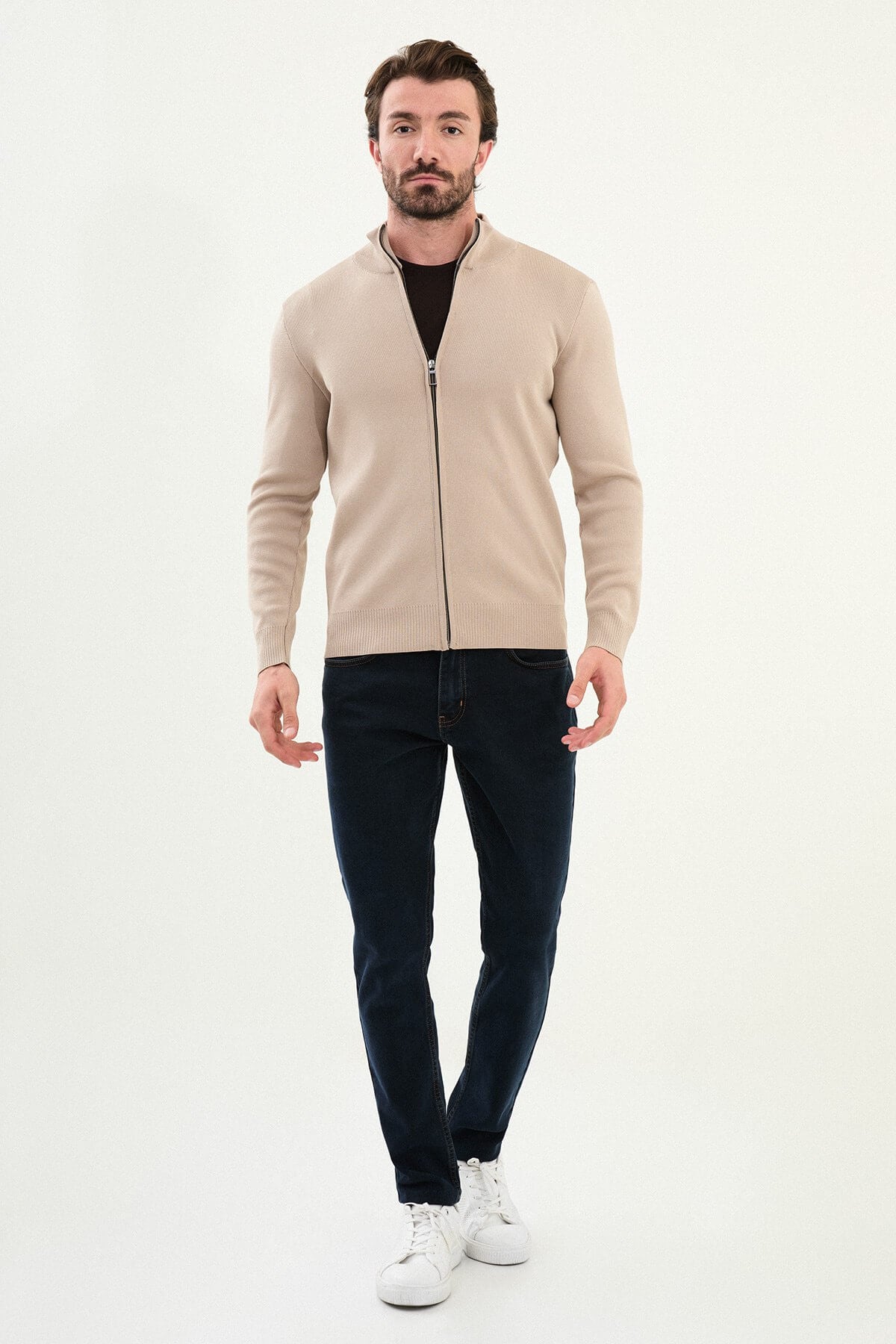 A man wearing a slim fit beige zip cardigan over a dark T-shirt, styled with dark navy jeans.