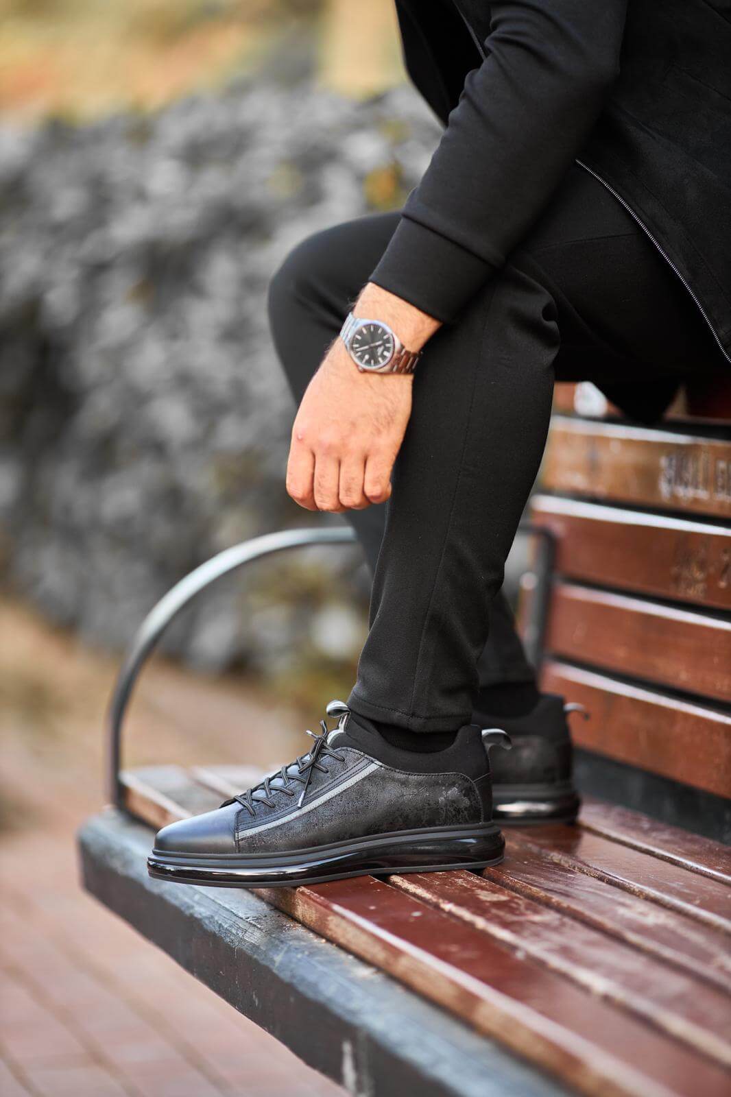 Black genuine leather sneakers with suede panels, worn with black trousers on outdoor wooden bench.