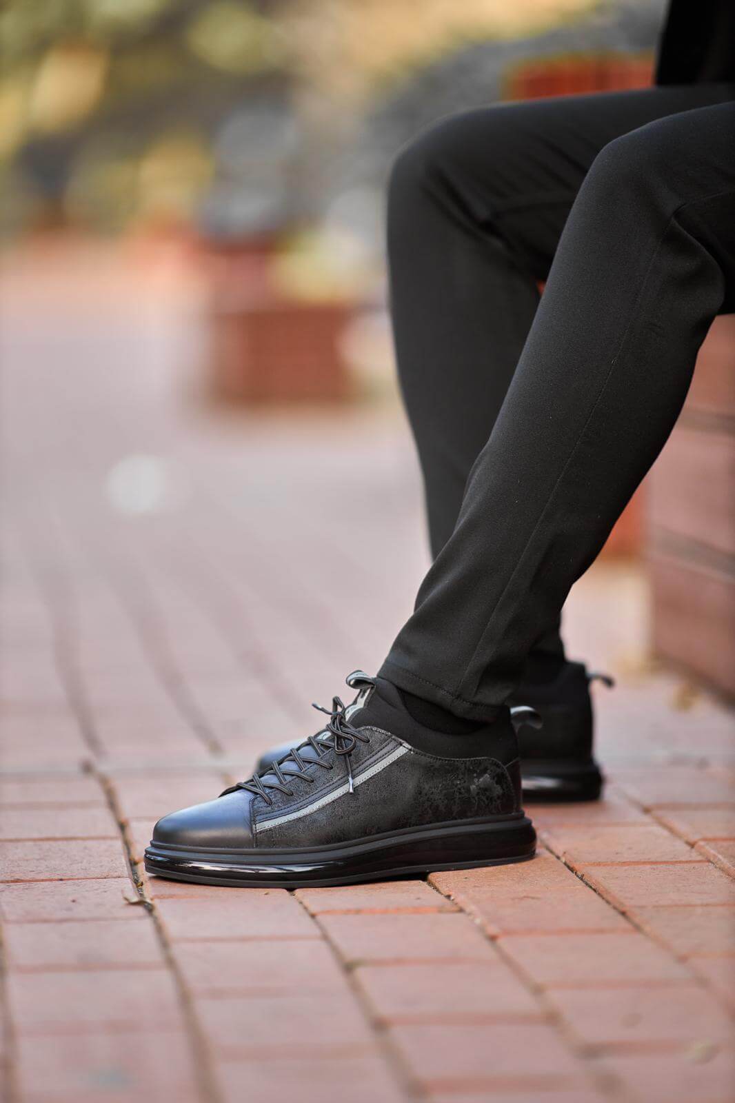 Black genuine leather sneakers with suede panels, worn with black trousers on outdoor wooden bench.