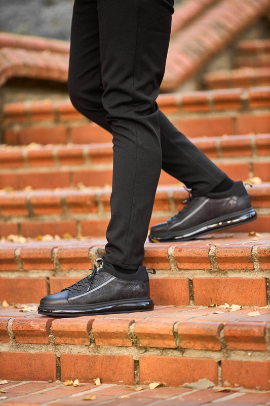Black genuine leather sneakers with suede panels, worn with black trousers on outdoor wooden bench.