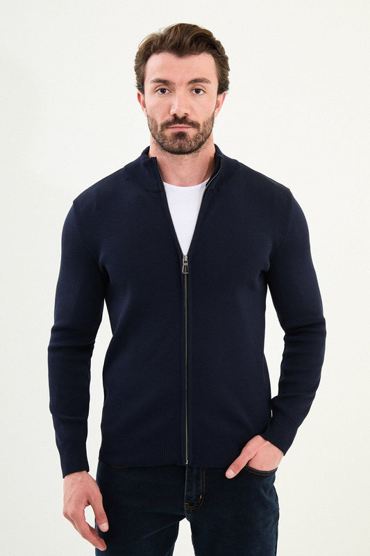 A man wearing a slim fit navy blue zip cardigan with a stand-up collar, styled with a white T-shirt and dark jeans.