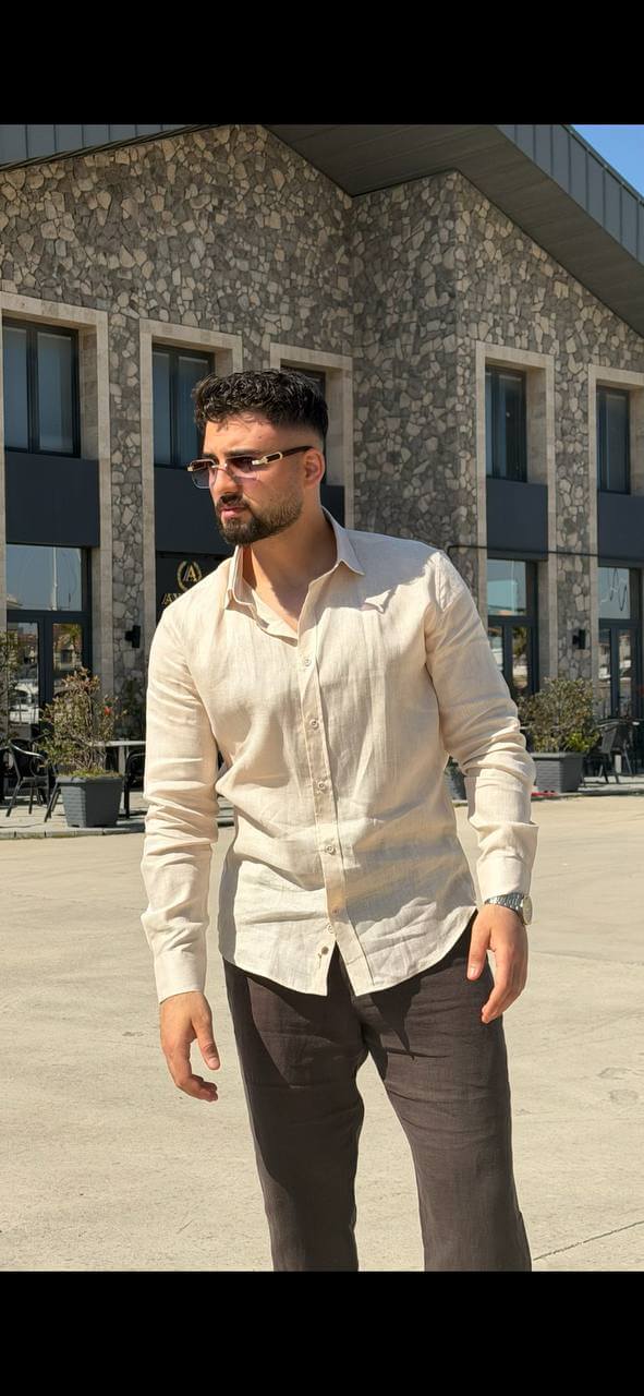 Man wearing a beige linen long-sleeve collared shirt, standing outdoors with a casual fit, styled with dark trousers.