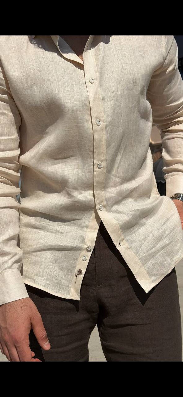 Man wearing a beige linen long-sleeve collared shirt, standing outdoors with a casual fit, styled with dark trousers.