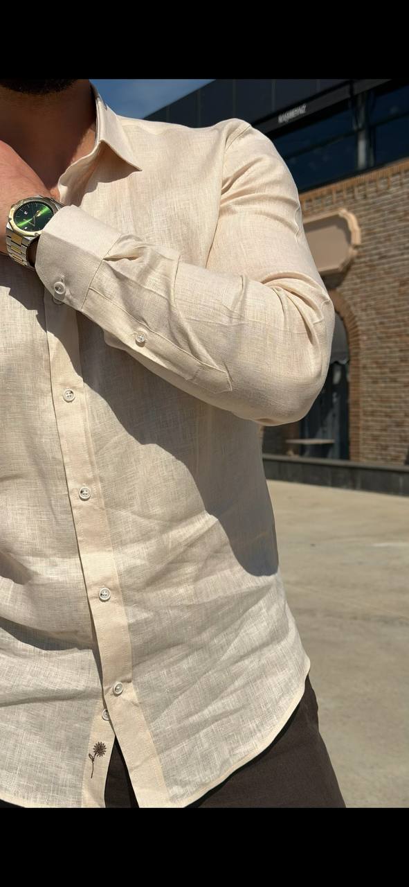 Man wearing a beige linen long-sleeve collared shirt, standing outdoors with a casual fit, styled with dark trousers.