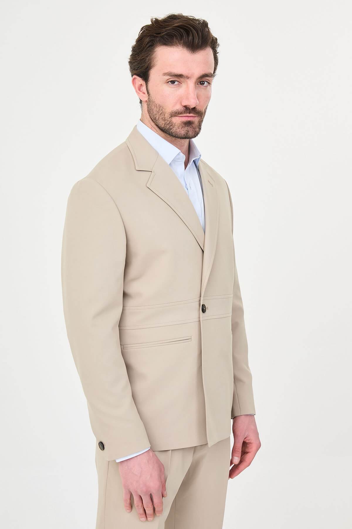 Man wearing a slim fit beige suit with notch lapel, paired with dress shoes.